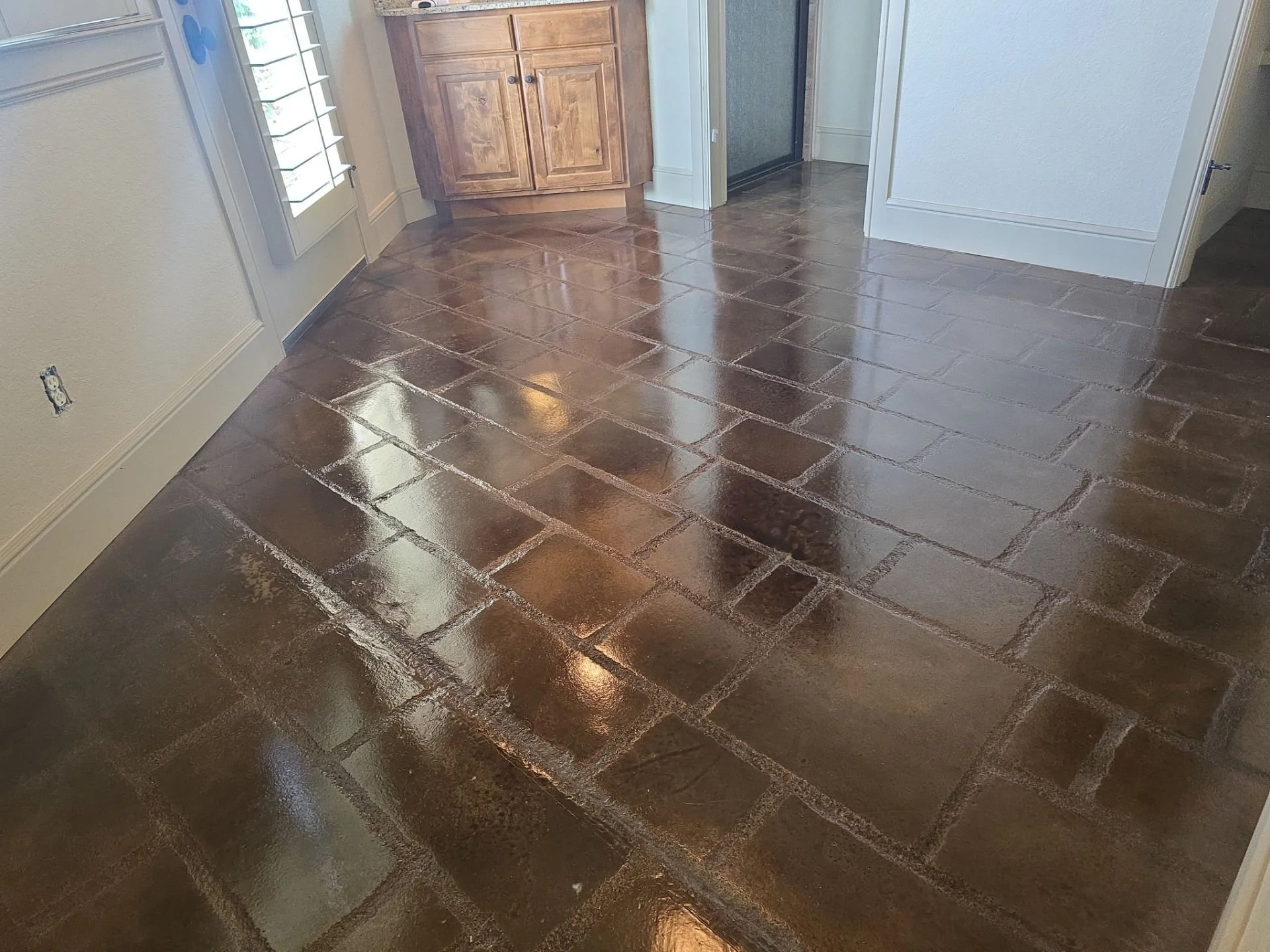 Shiny brown tiles on a kitchen floor with a corner cabinet and a door in the background.