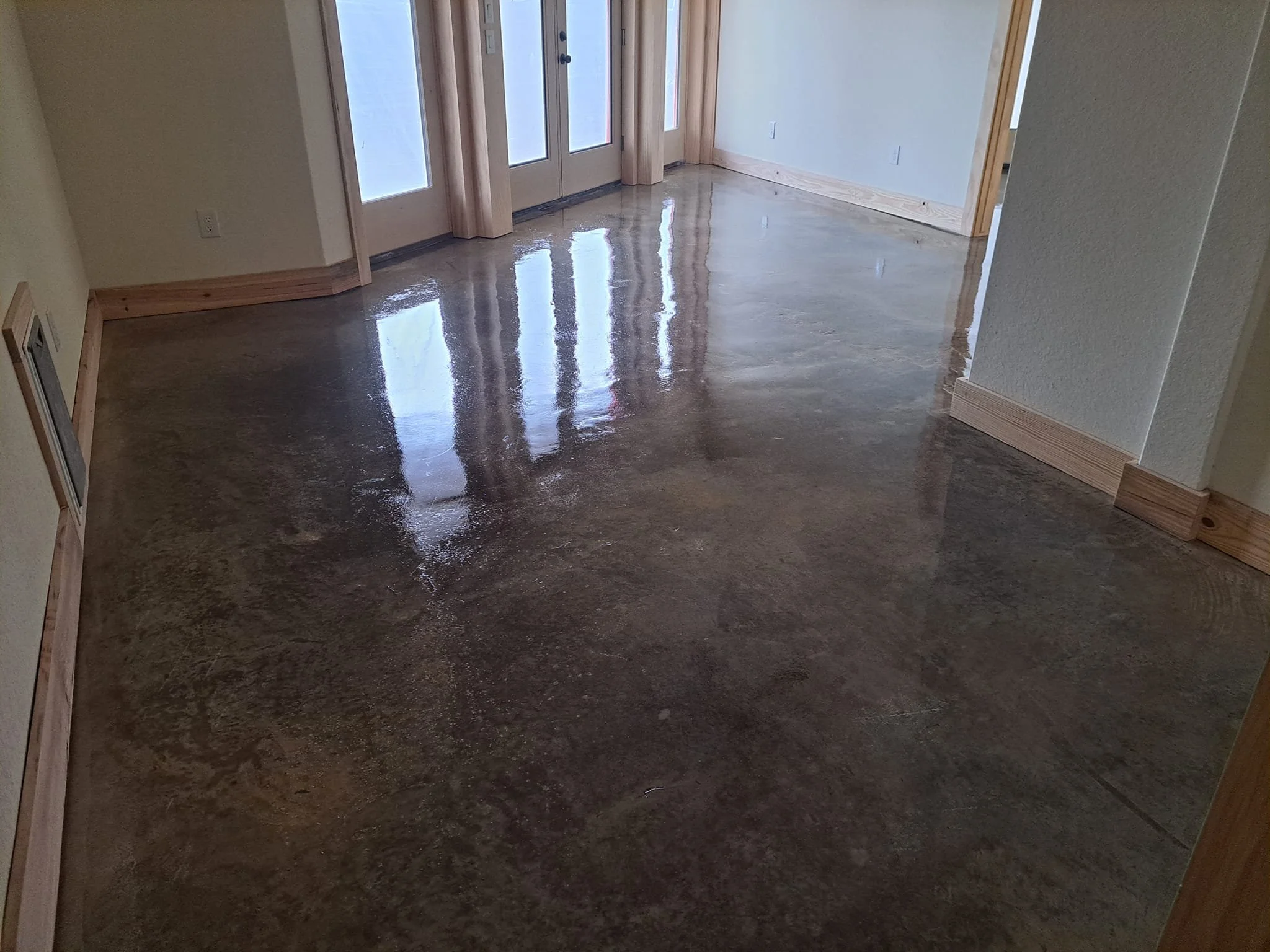 Photo of a shiny, polished concrete floor inside a house near a set of French doors with glass panes.