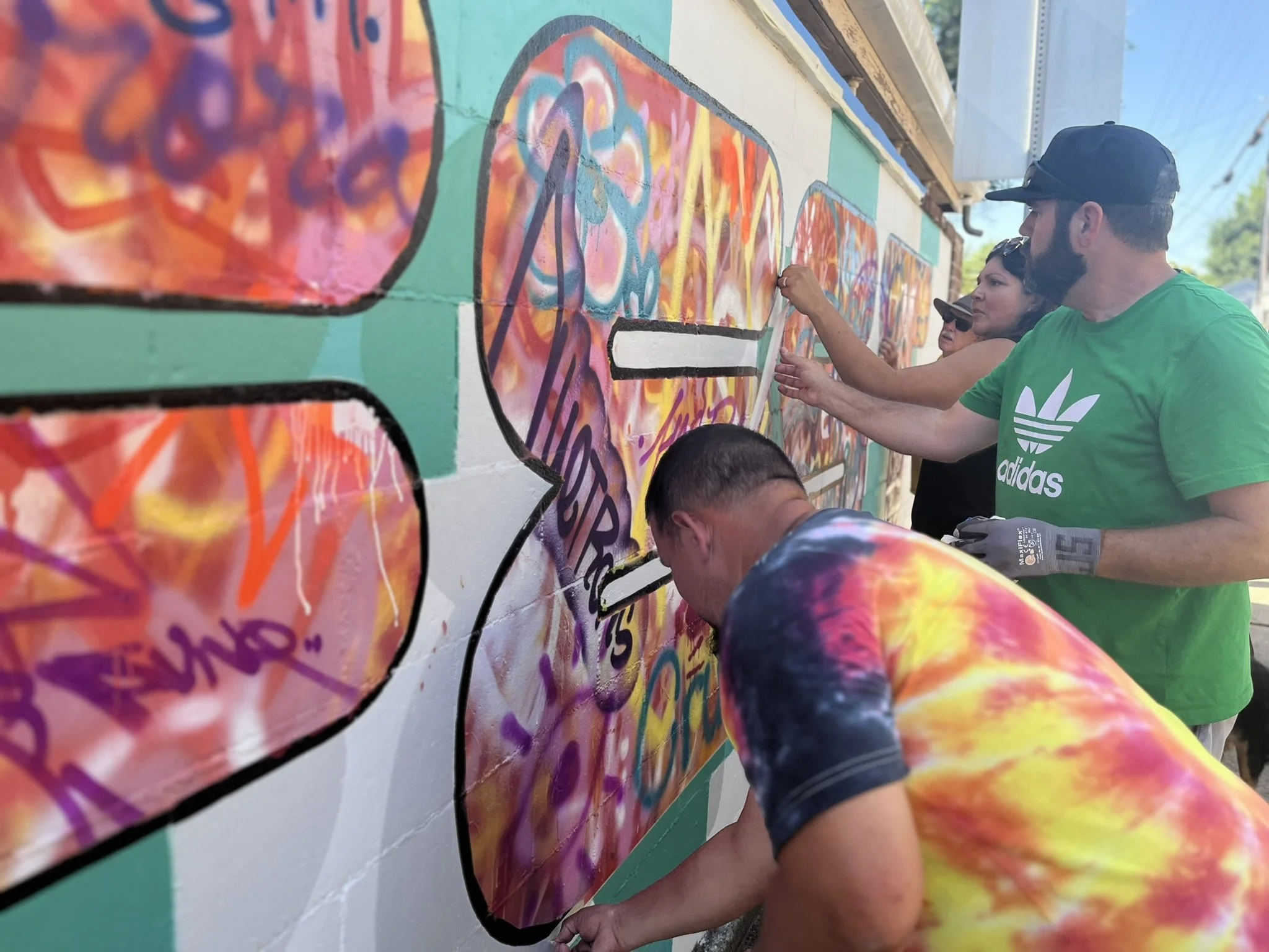 People painting a colorful graffiti mural on a wall outdoors.