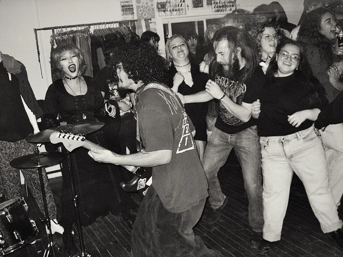 Frontman of Maiden Lane playing guitar for a crowd of people who are enjoying the punk rock show. Shot in black and white.