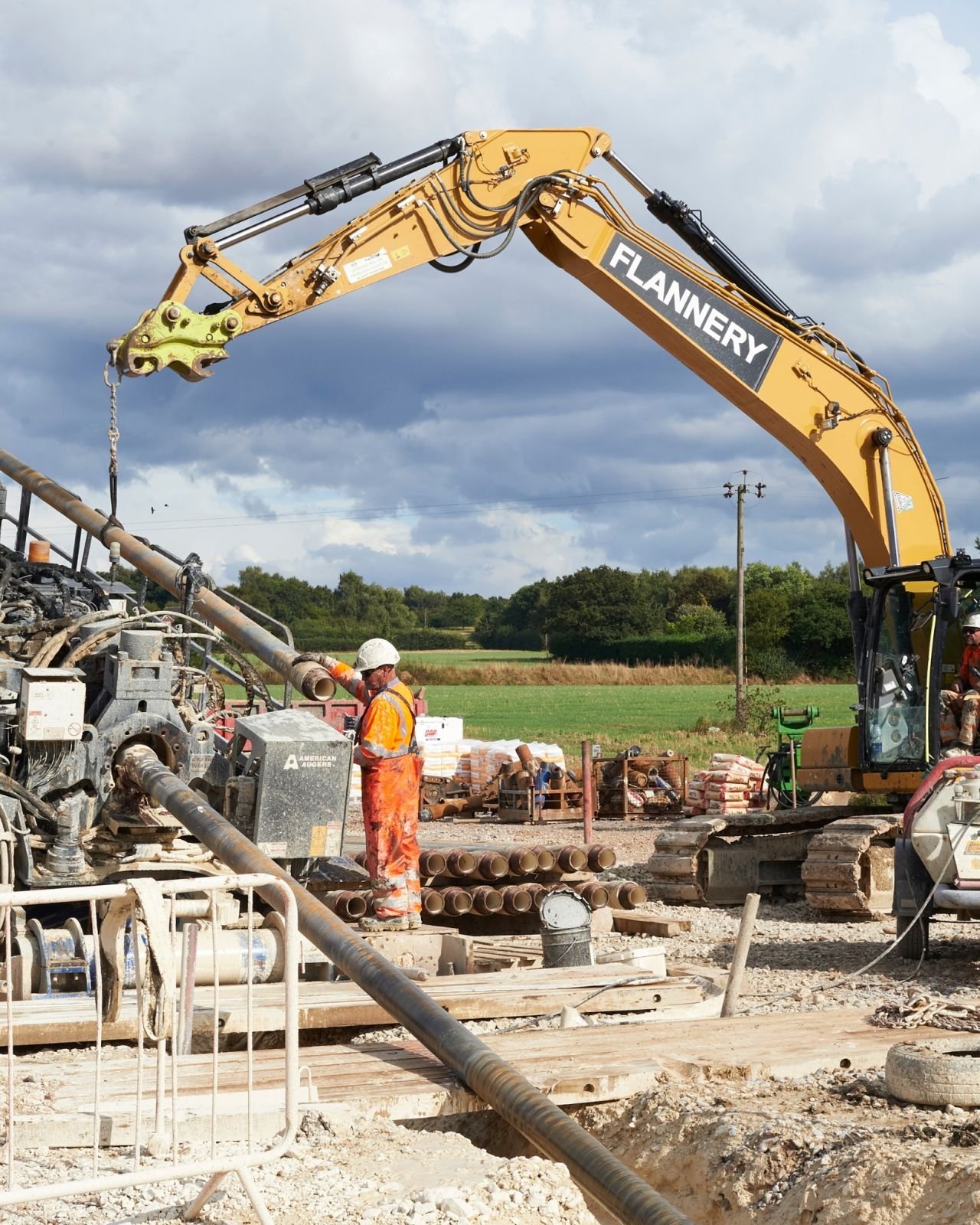 Construction workers and heavy machinery working on a project outdoors, with excavation equipment and pipes visible.