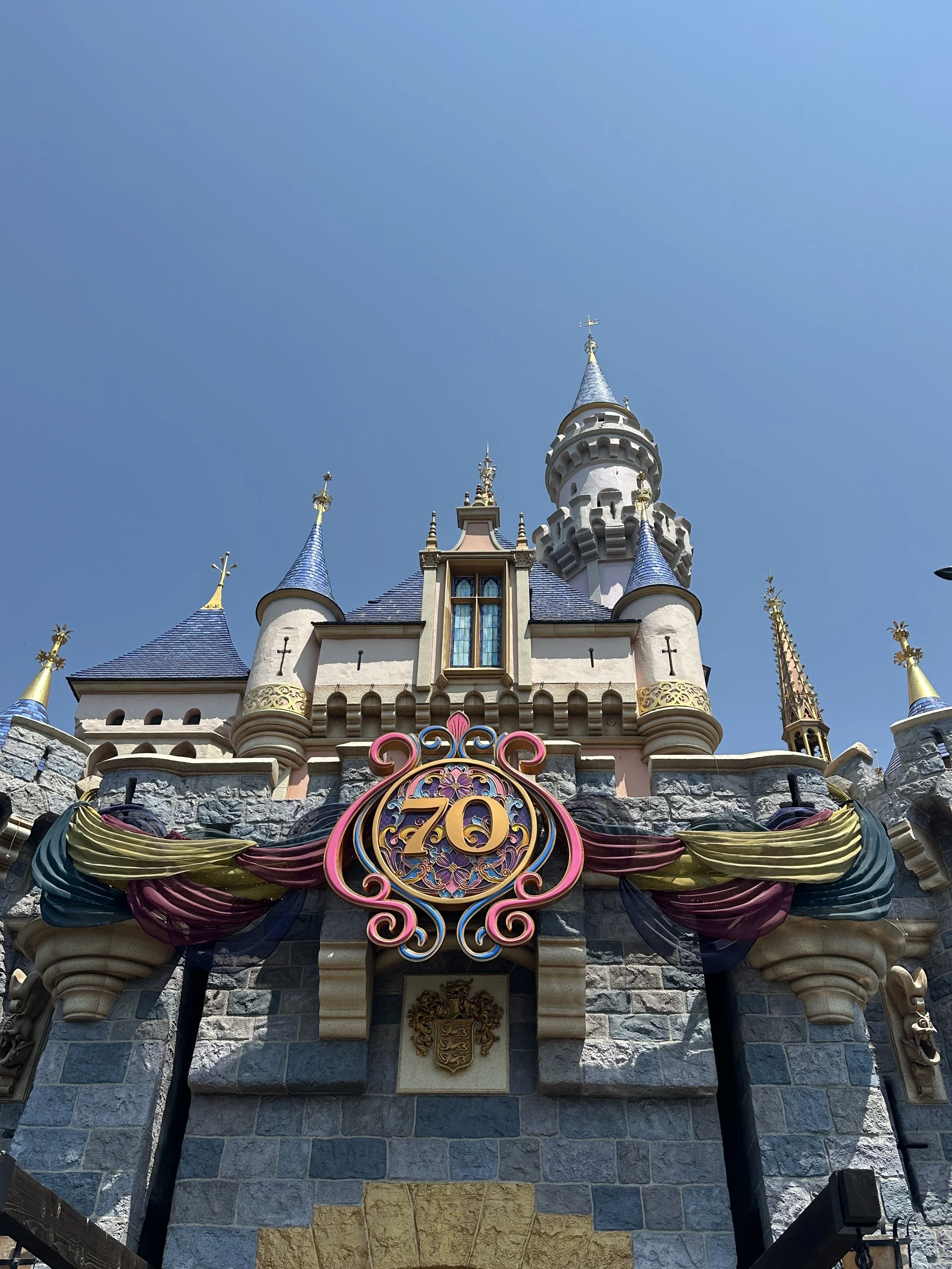 Sleeping Beauty Castle decorated for the 70th anniversary at Disneyland with colorful banners and a castle spire against a clear blue sky.