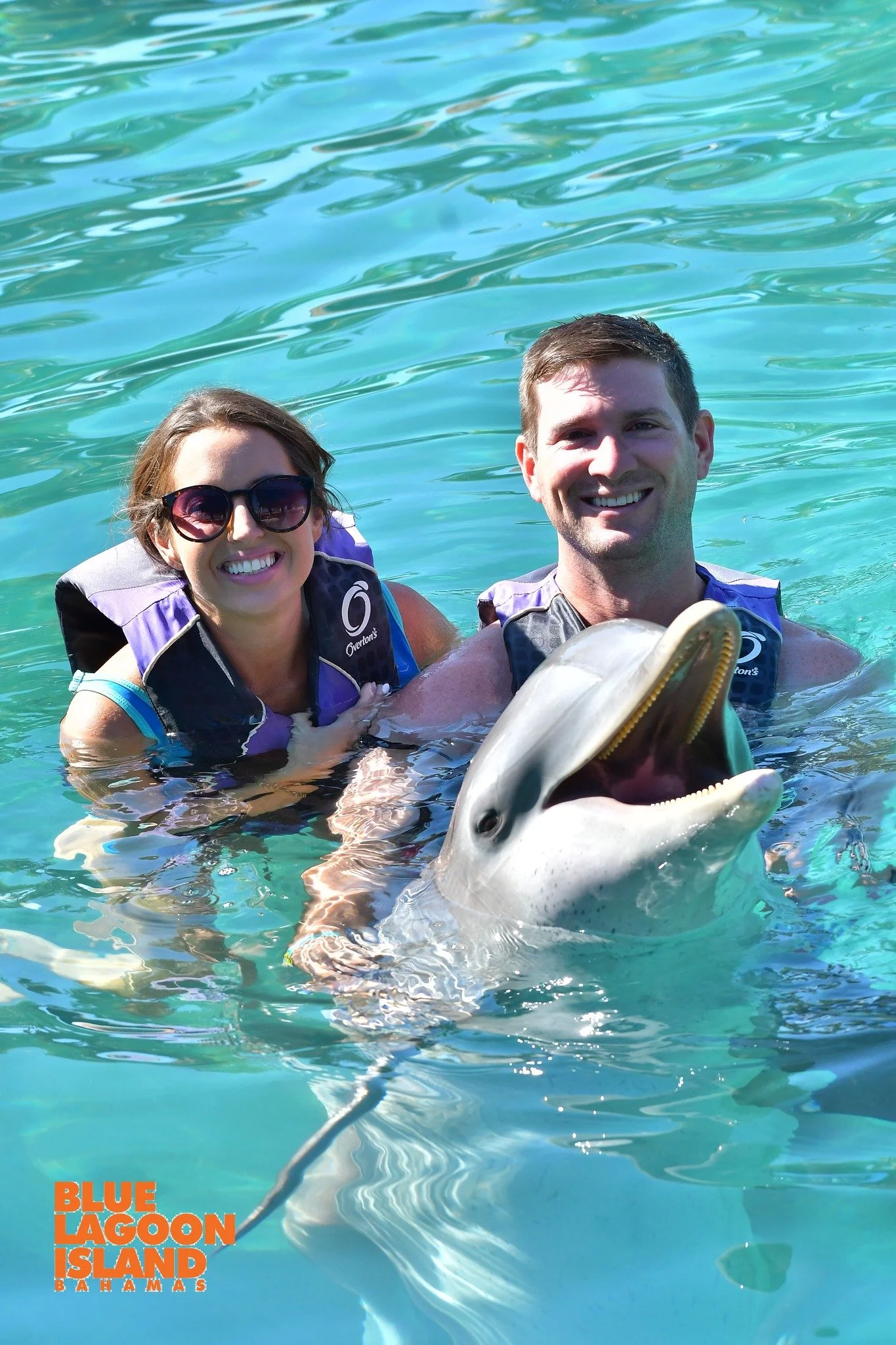 Two people smiling in the water with a dolphin at Blue Lagoon Island in the Bahamas.