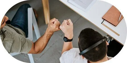 Two people sitting at a white table, one wearing a smartwatch, with notebooks on the table.