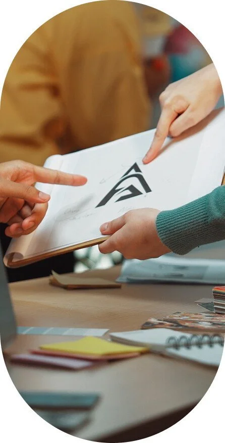 People examining a booklet with a black and white logo on the open page, pointing at it.