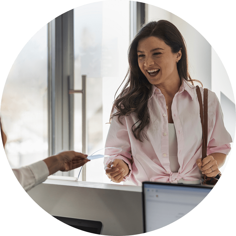 A woman smiling and laughing while checking into a building and receiving a card from a person behind a reception desk.