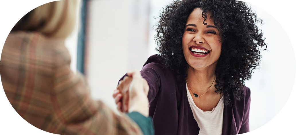 Two women shaking hands, smiling and happy, in a professional setting.