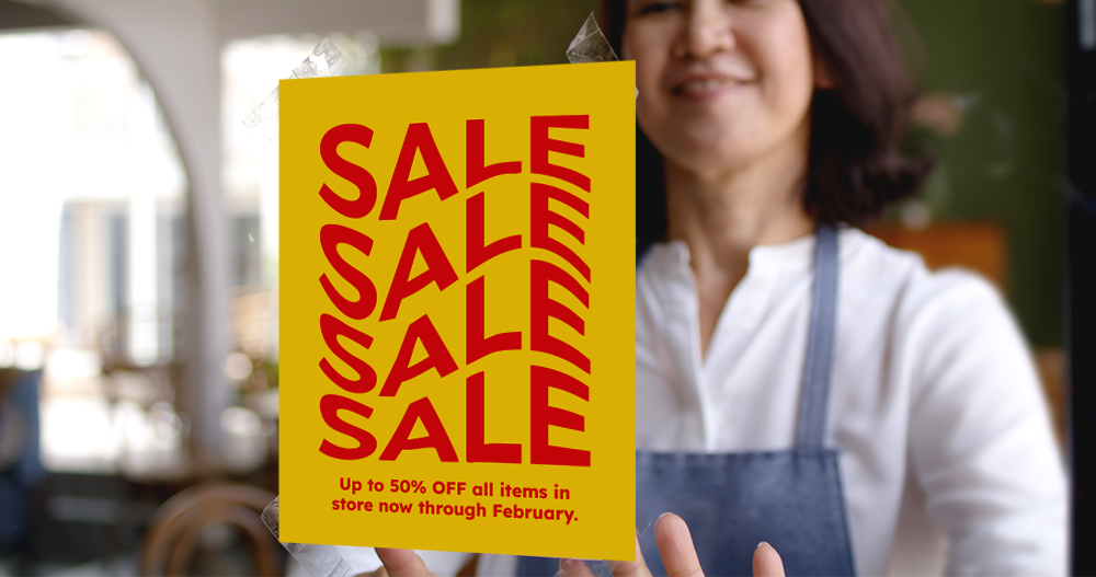 A woman in an apron holding a yellow sign with red text that says 'SALE' multiple times and announces up to 50% off on all items through February.