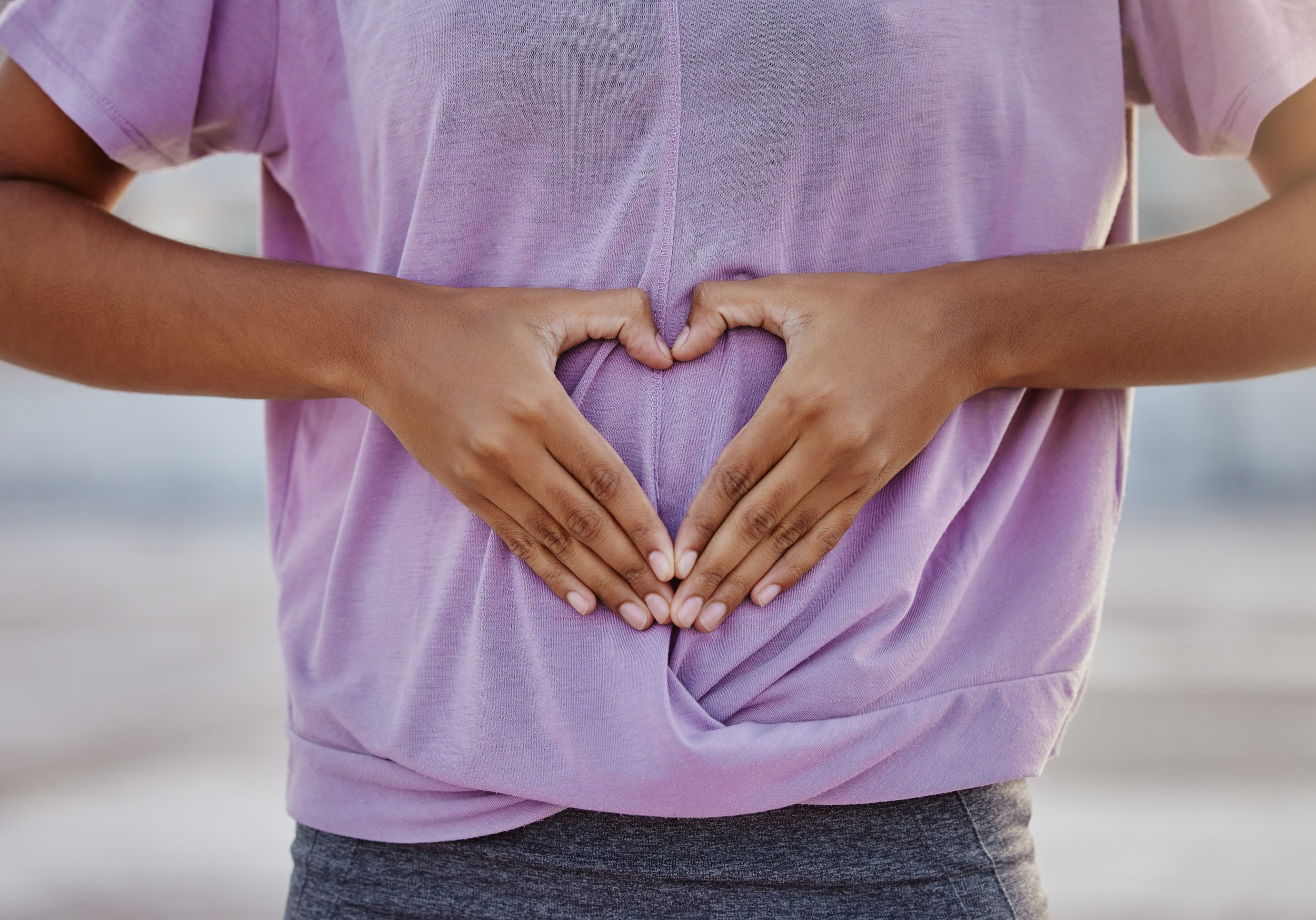 Person wearing a purple t-shirt making a heart shape with hands on stomach
