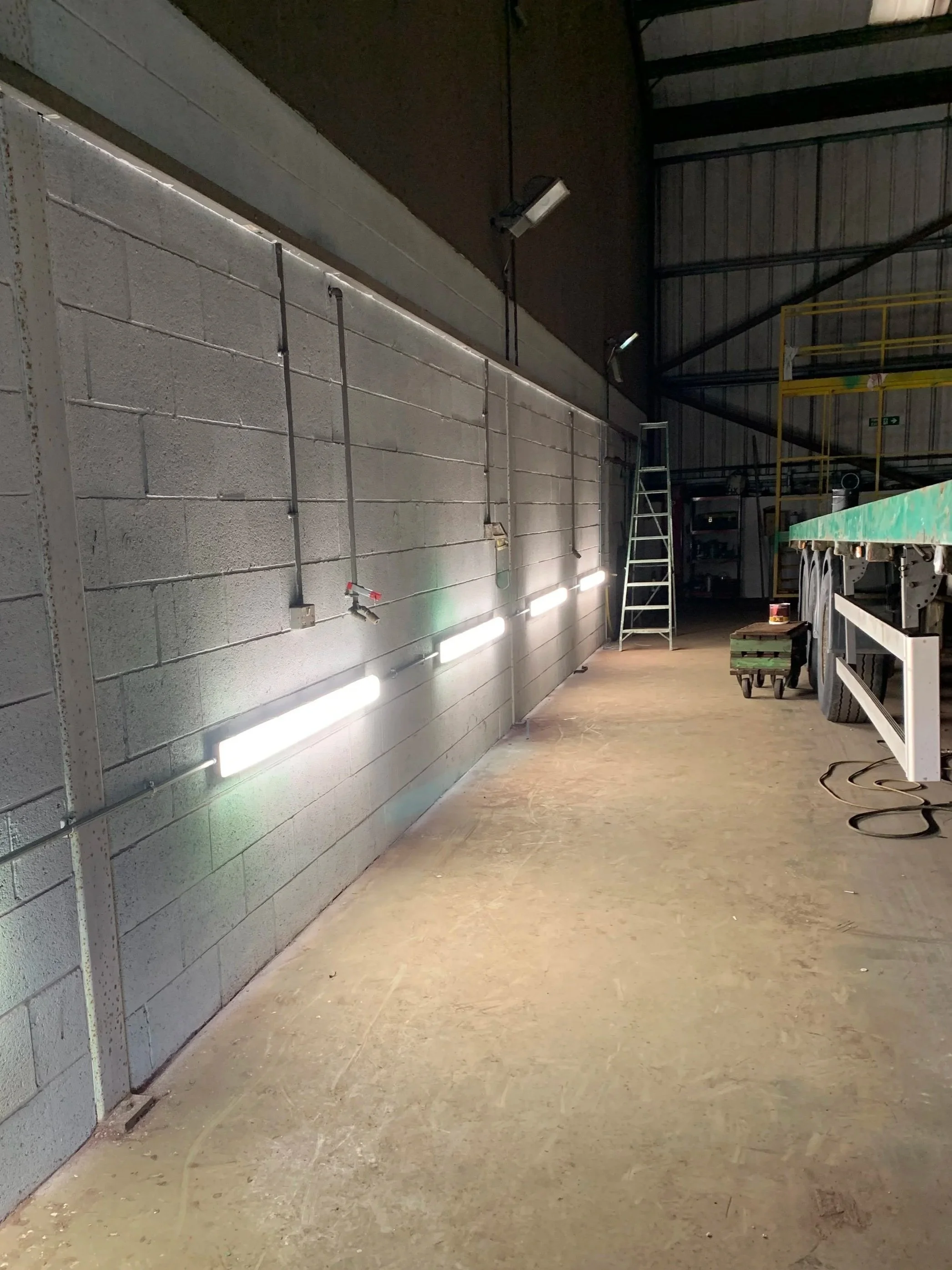 Construction inside a building with a concrete wall, metallic ladder, work lights, and construction materials on the ground.