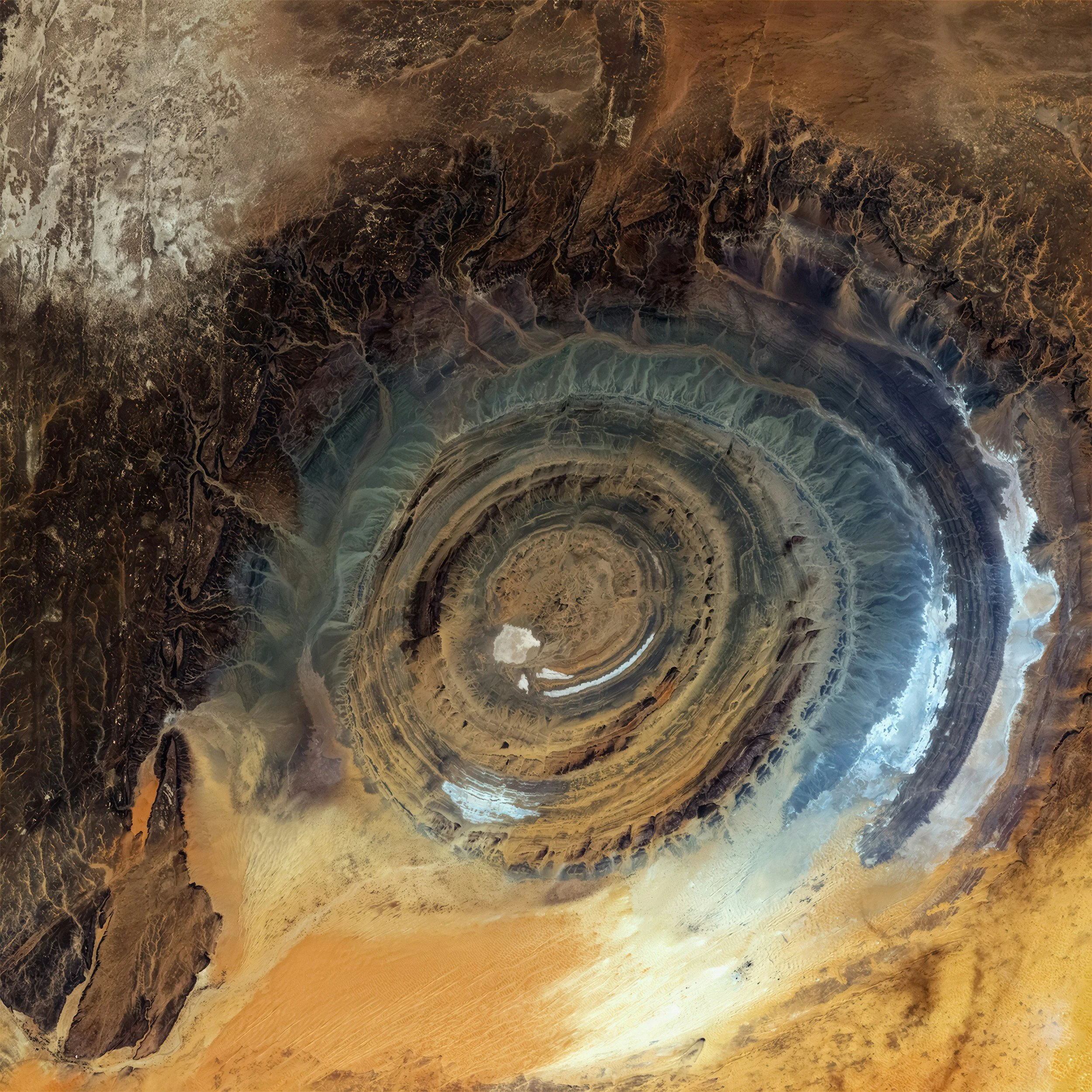 Satellite view of a giant, circular salt pan with concentric rings, surrounded by arid desert landscape.