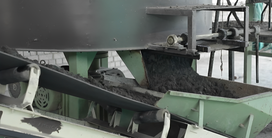 A factory or industrial setting with machinery processing a dark material, possibly coal or ore, into a conveyor belt system.