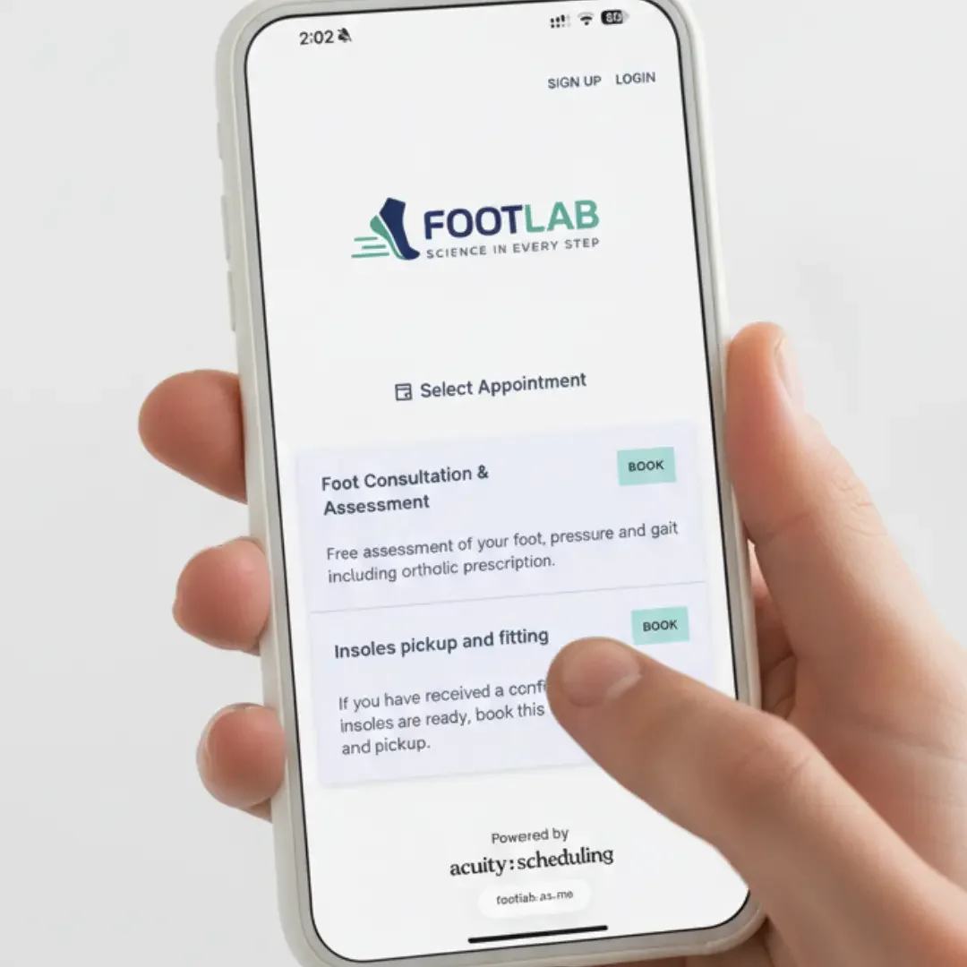 A person holding a smartphone displaying the FootLab appointment booking app, with options for foot consultation and insoles fitting services.