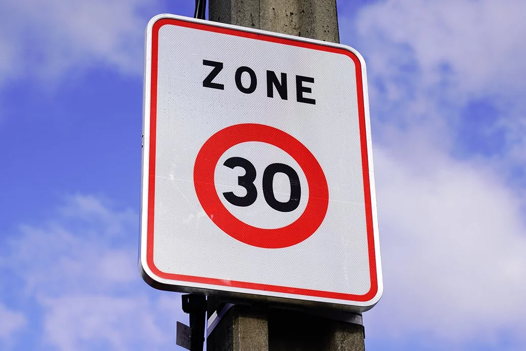 Un panneau de limite de vitesse indiquant une zone de 30 km/h avec un fond blanc, une bordure rouge et le texte 'ZONE 30'.