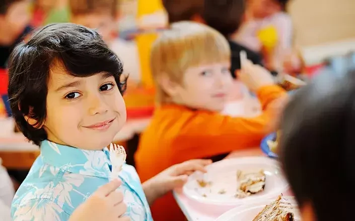 Groupe d'enfants souriants en train de déjeuner dans une salle de classe ou une cafétéria