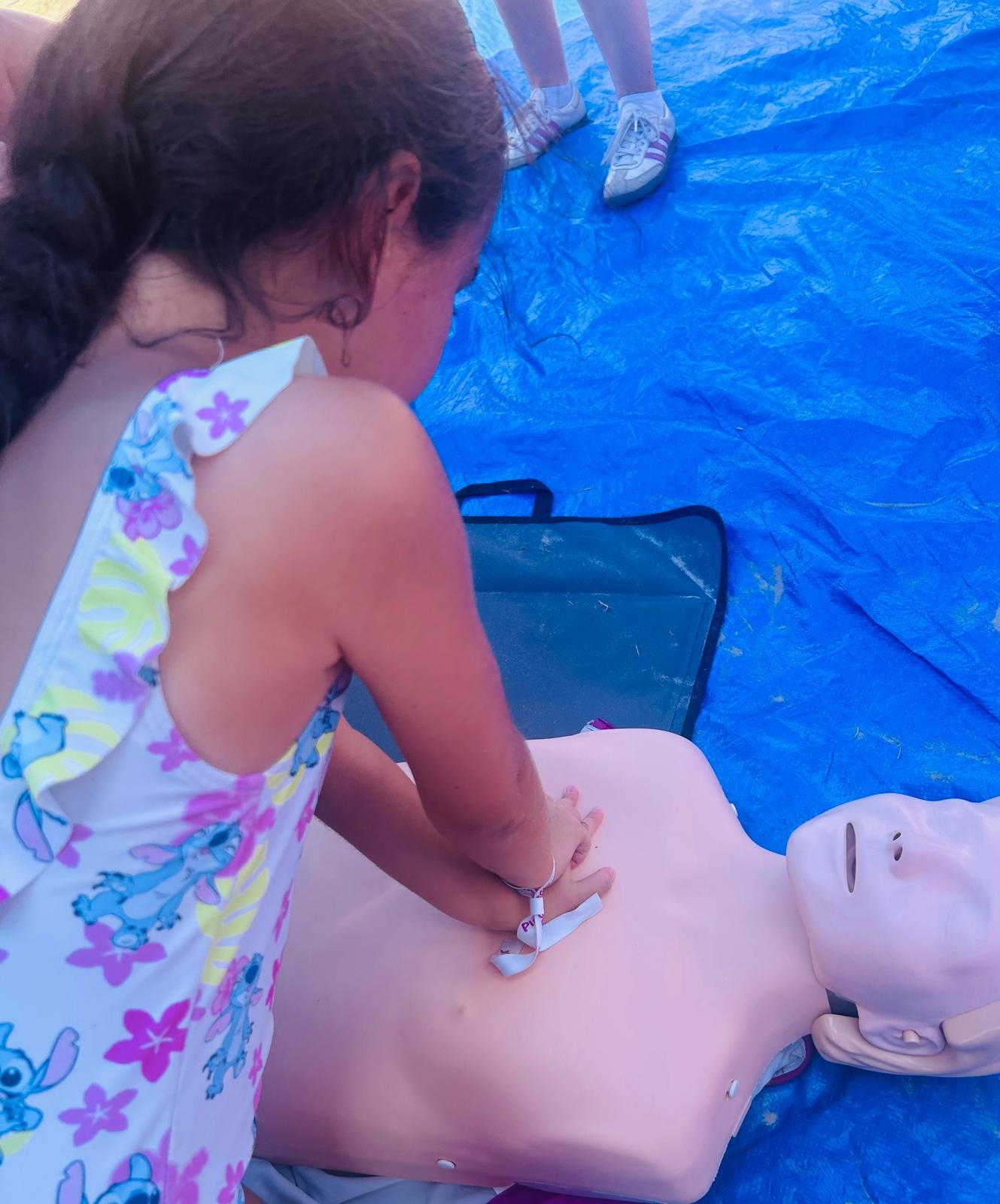 Une femme effectue un massage cardiaque sur un mannequin de formation médicalisée, installé sur une surface recouverte d'une toile bleue, lors d'une séance de formation aux premiers secours.