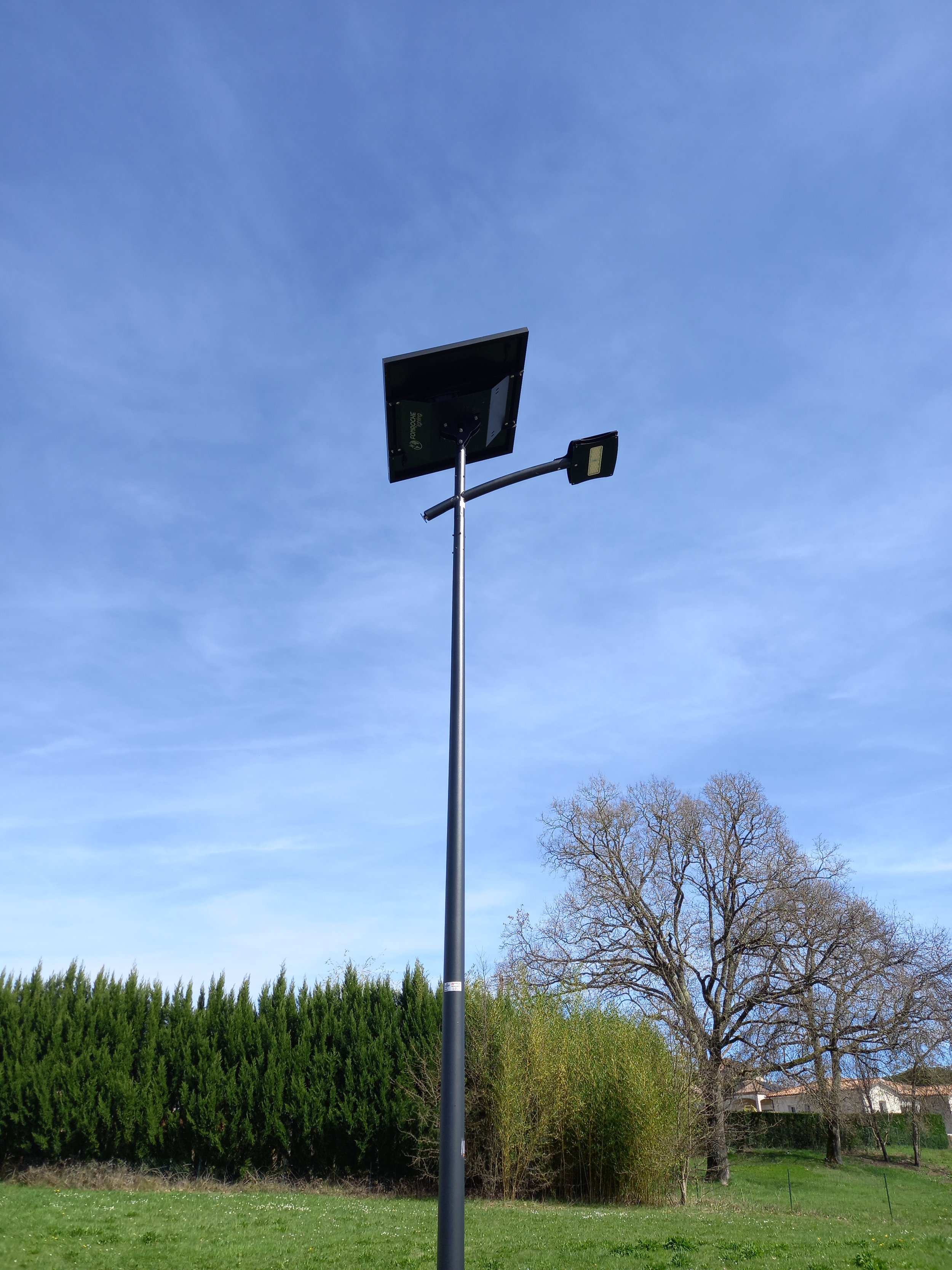 Un lampadaire futuriste avec panneaux solaires et lampe LED dans un parc avec des arbres en arrière-plan et un ciel clair.