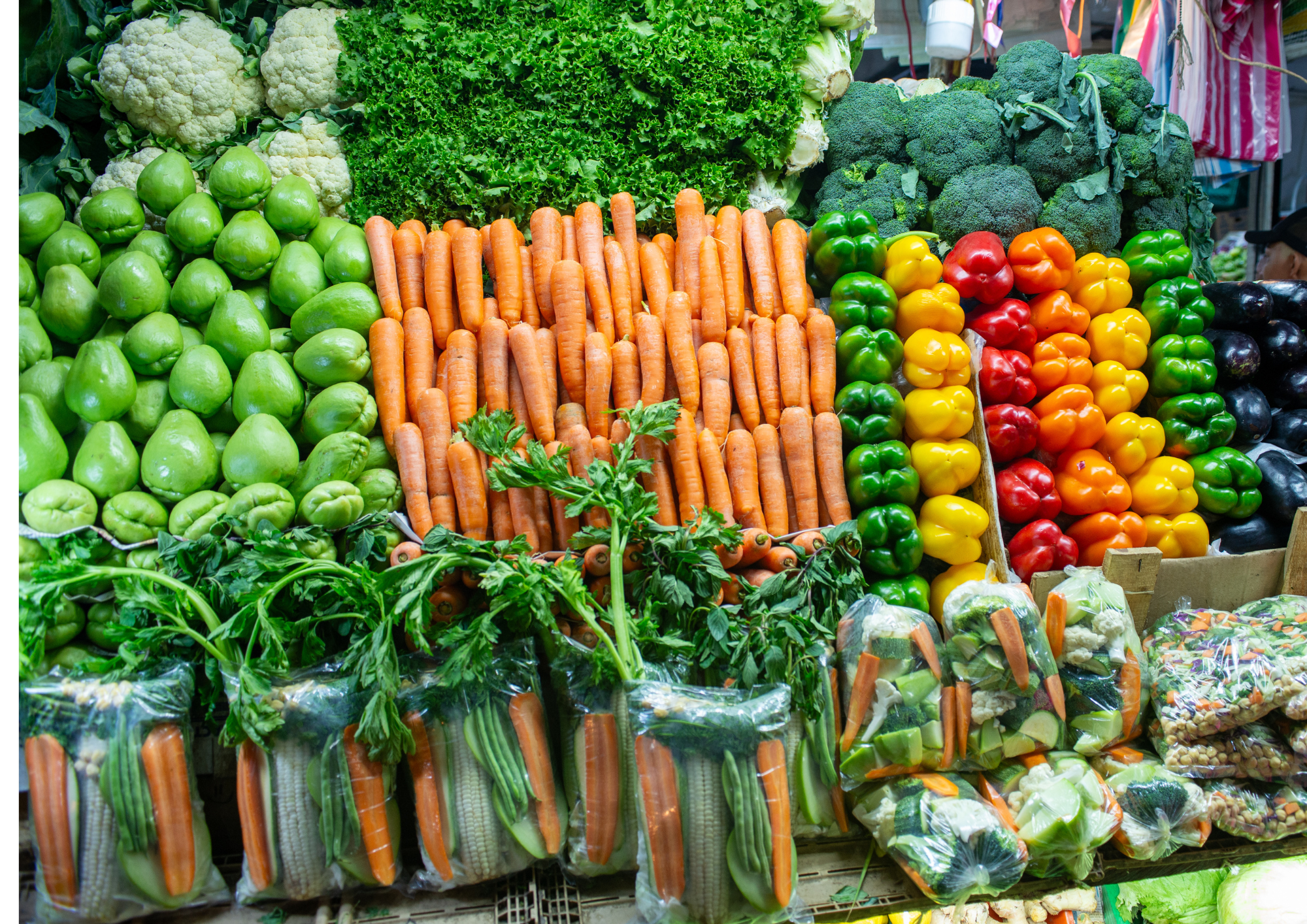 Légumes frais tels que choux-fleurs, carottes, brocolis, poivrons verts, jaunes, rouges et oranges, aubergines, et autres légumes emballés en sac dans un marché
