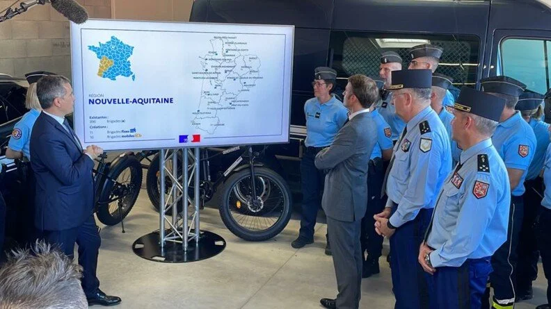 Un groupe de policiers en uniforme assiste à une présentation ou à une réunion organisée par un homme en costume, devant un grand écran affichant une carte de la région Nouvelle-Aquitaine en France, avec un vélo visible en arrière-plan.