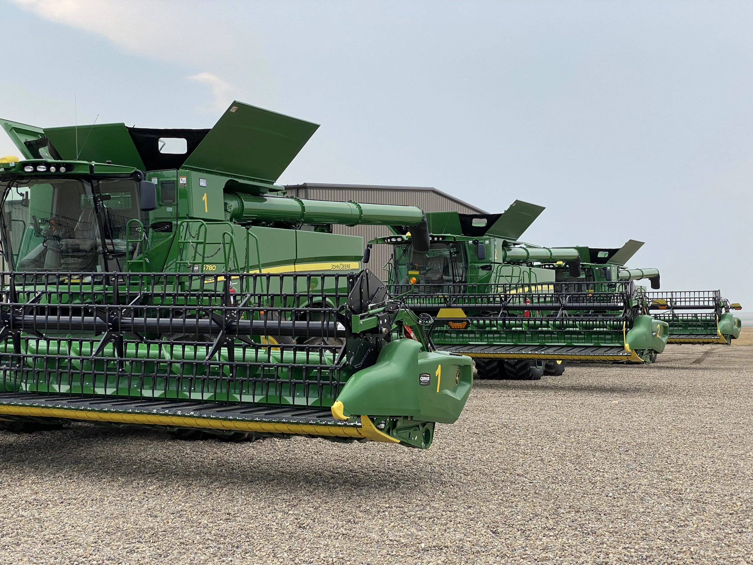 Three large green John Deere combine harvesters parked on a gravel surface.