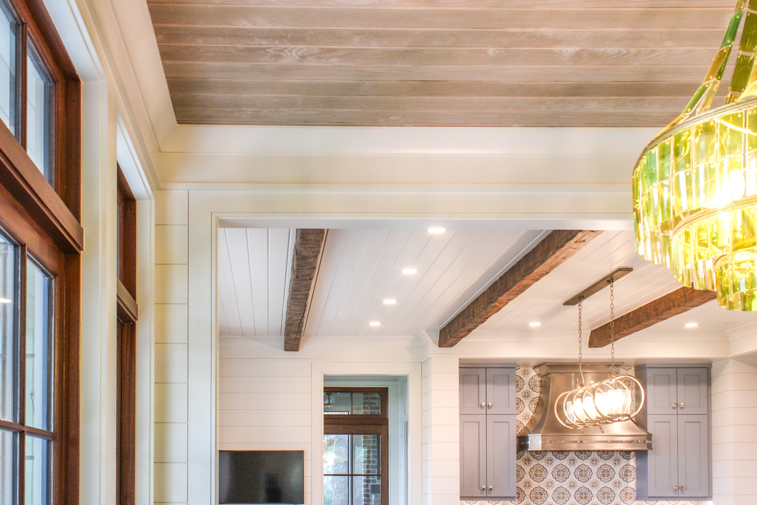 Interior view of a kitchen with wood beams on the ceiling, a hanging light fixture, and a television.