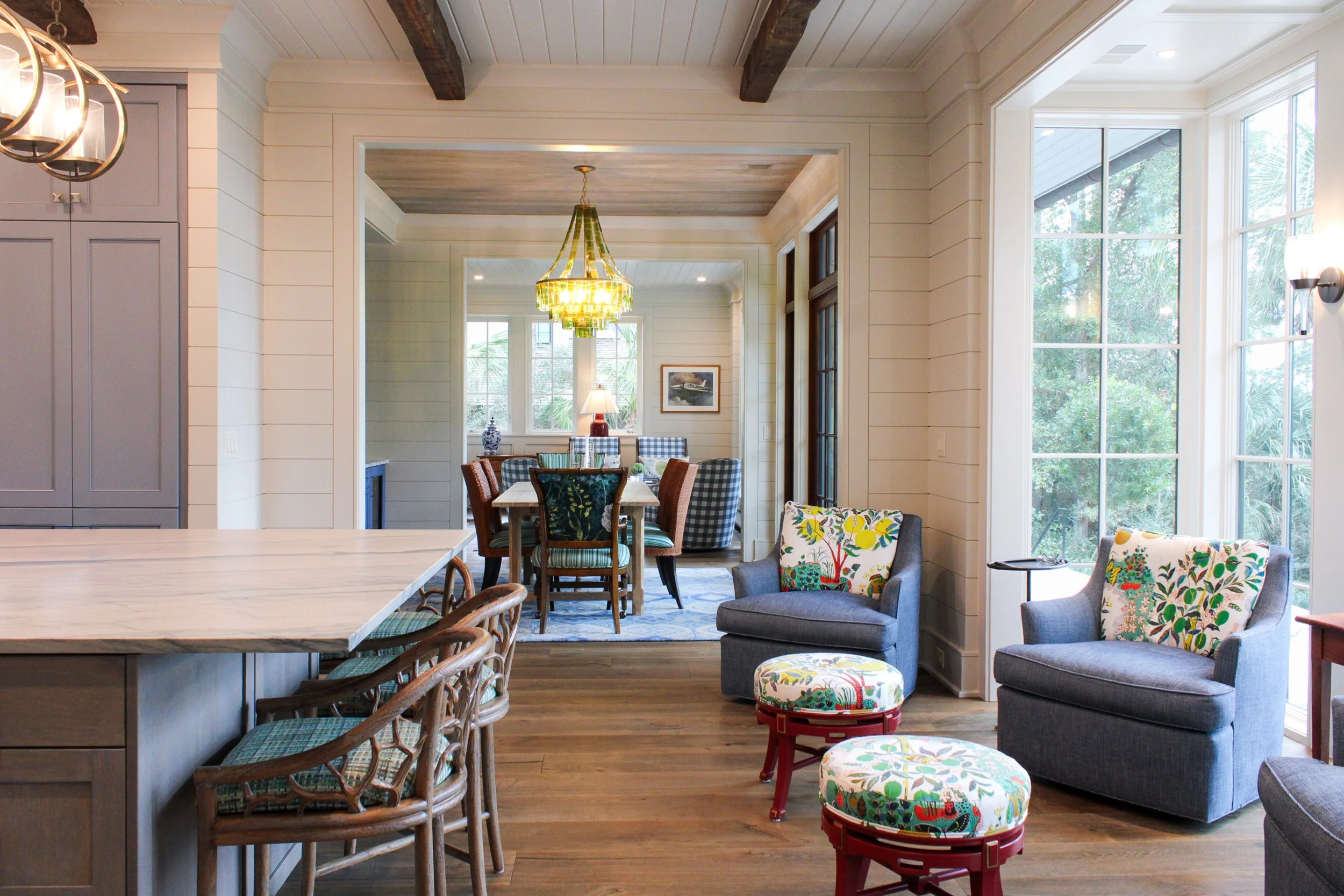 A bright open-concept living and dining area with large windows, hardwood floors, and a mix of colorful chairs and sofas.