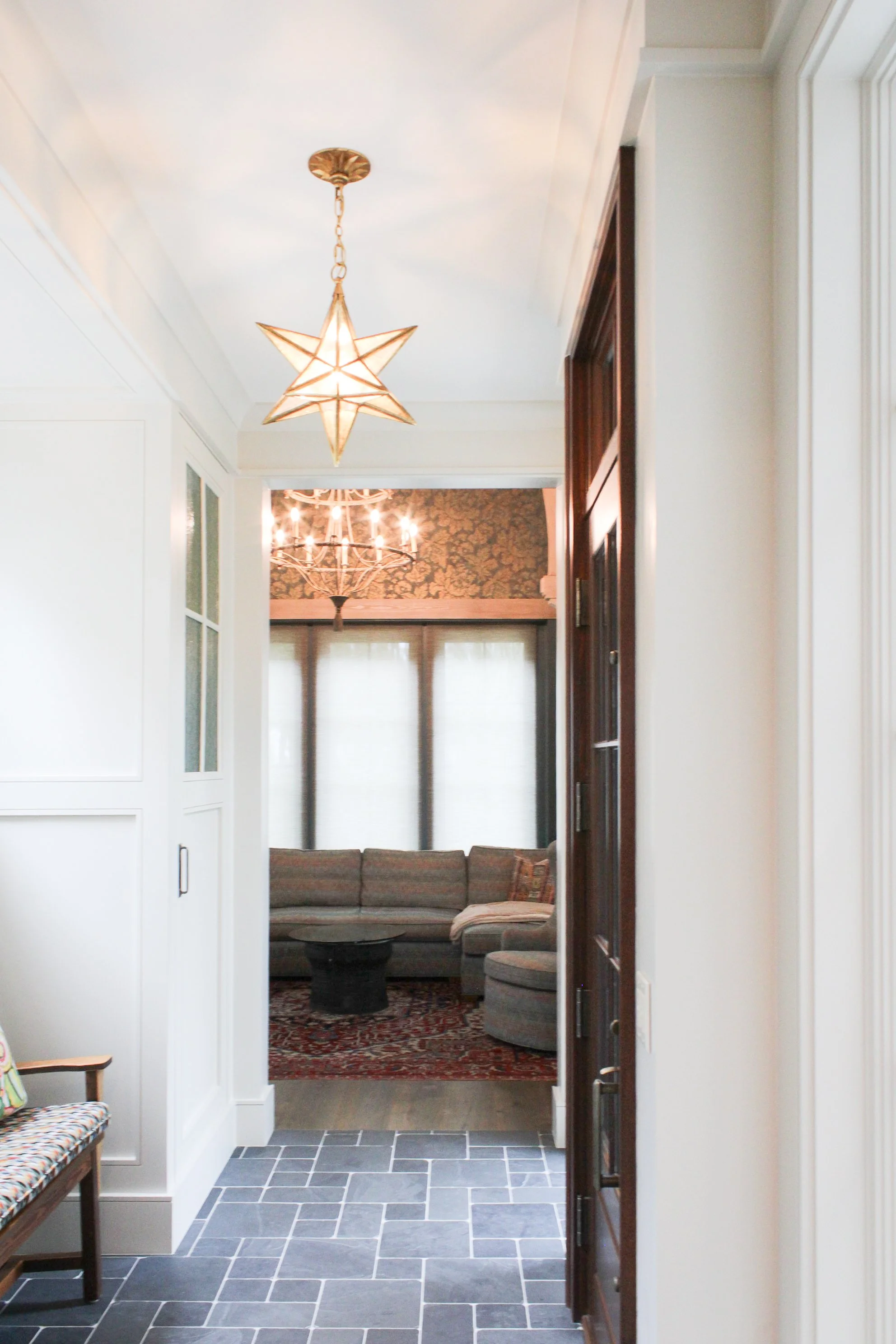 Entryway leading to a living room with a sectional sofa, chandelier, and patterned wallpaper.