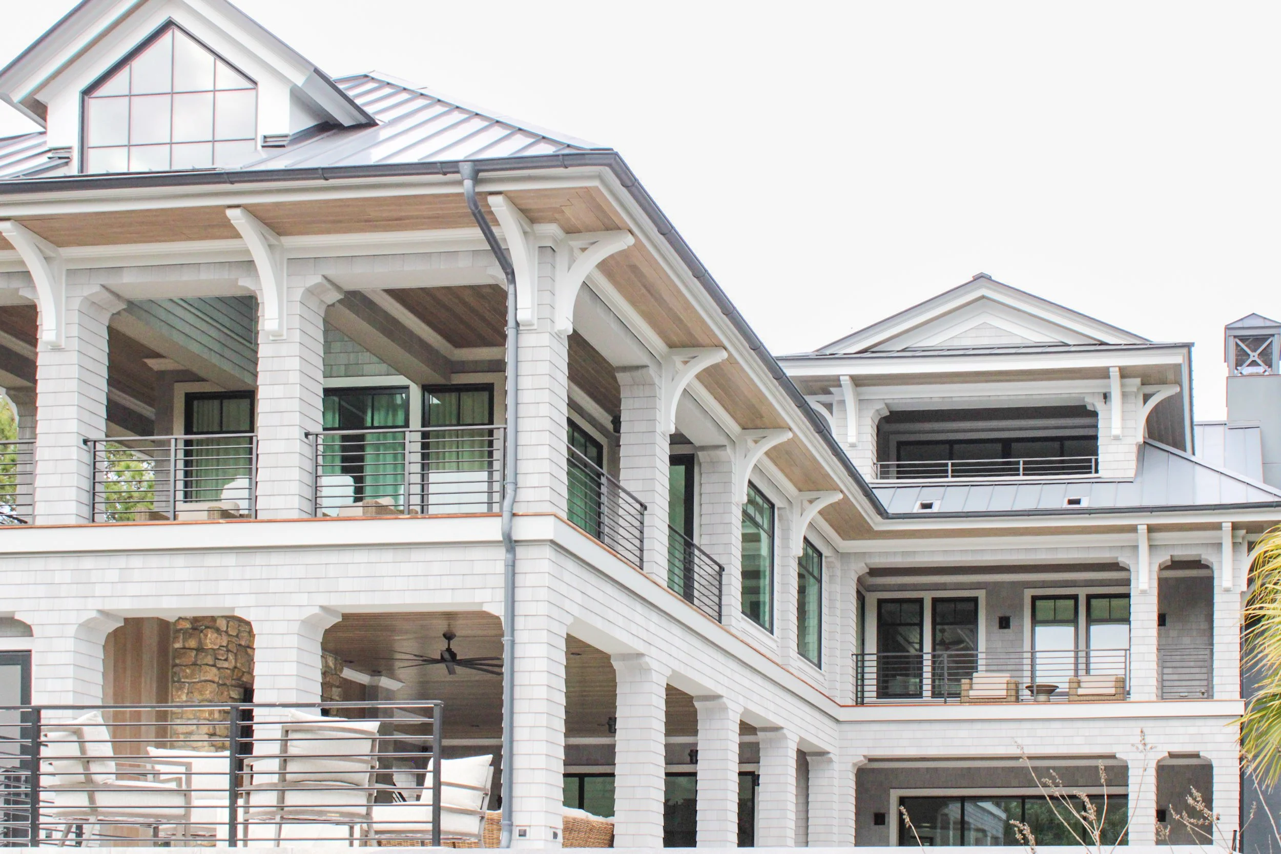 Multi-story modern house with white exterior, large windows, balconies, and a metal roof.