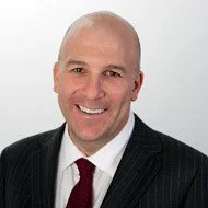 Portrait of a smiling man in a suit and tie with a white background.