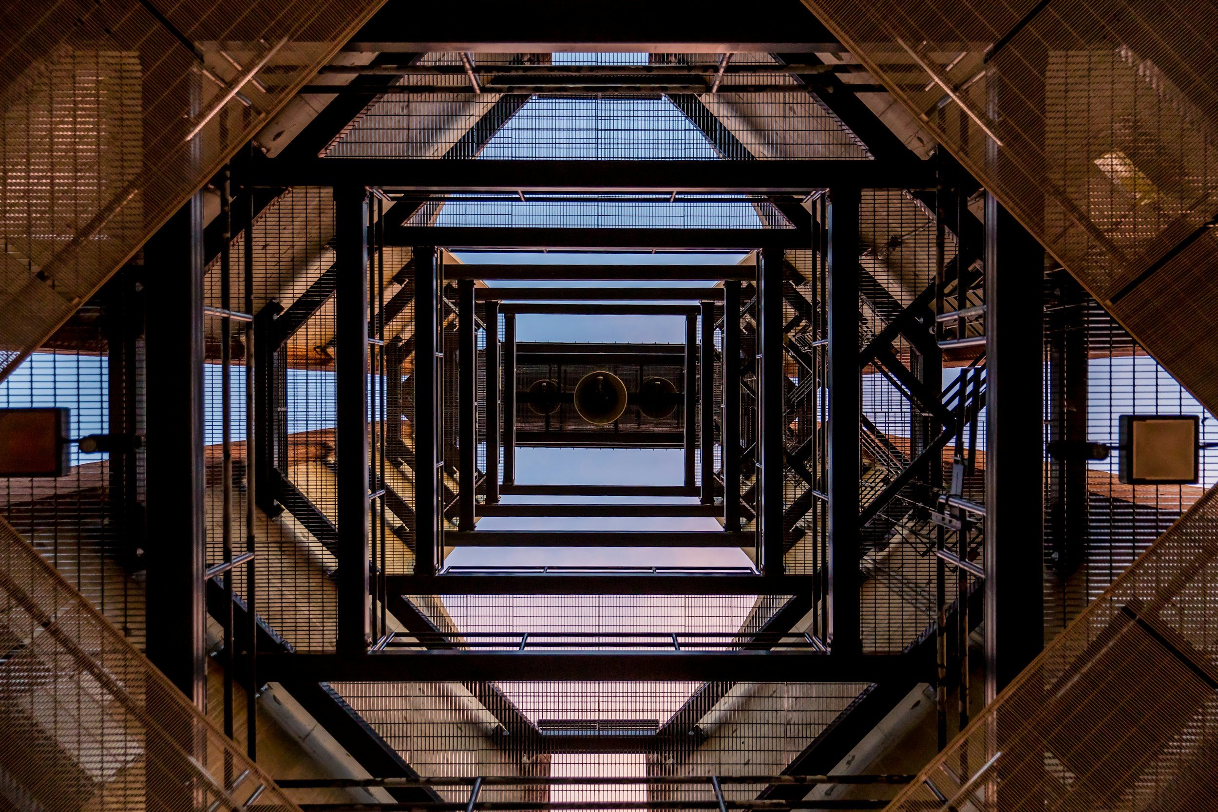 Looking up through a multi-level metal staircase with platforms and railings, showing the sky above.