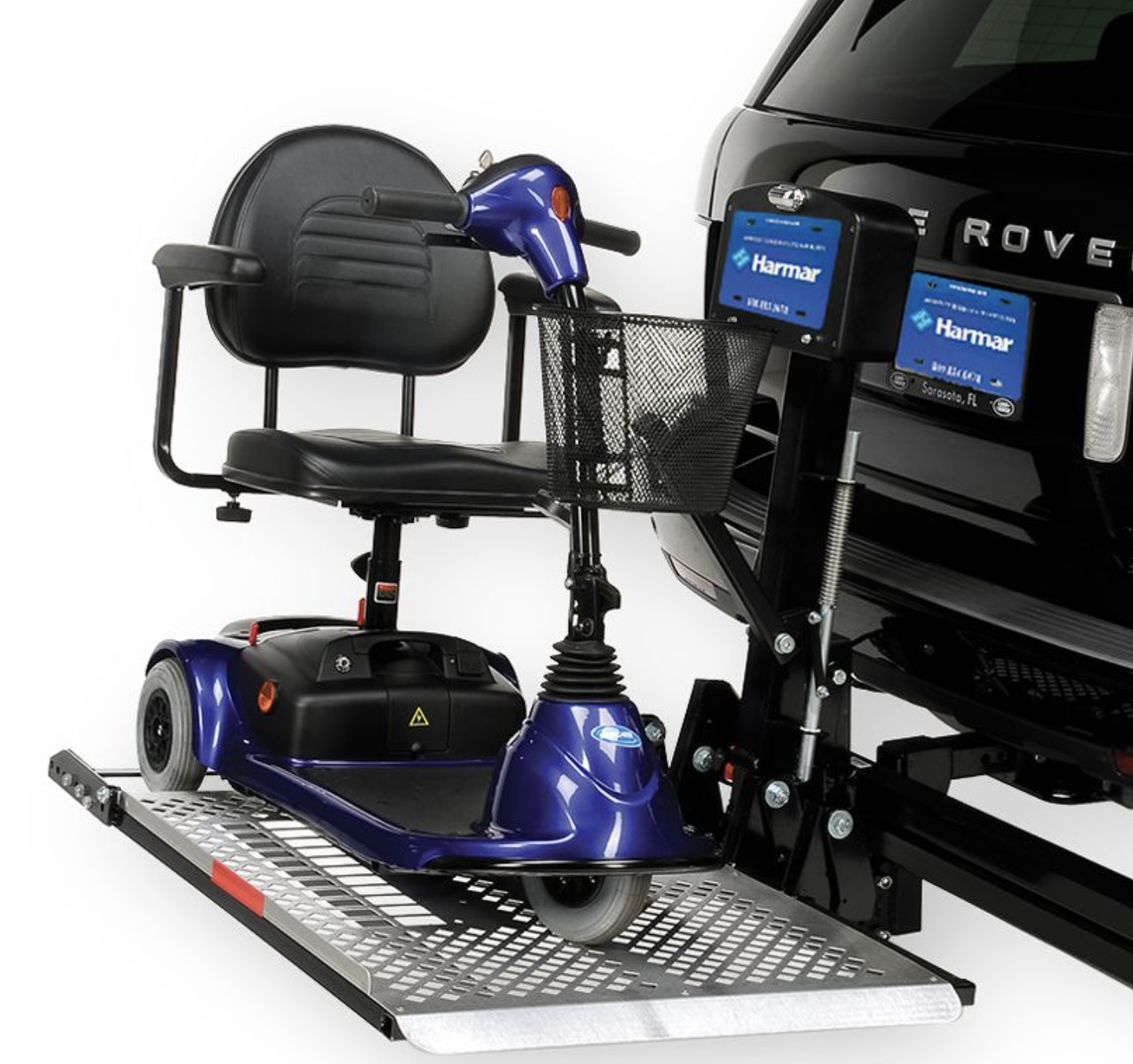 A vehicle onboard driving simulator equipped with a mobility scooter seat, steering controls, and two screens displaying Harmar branding, mounted on a metal platform with a black vehicle in the background.