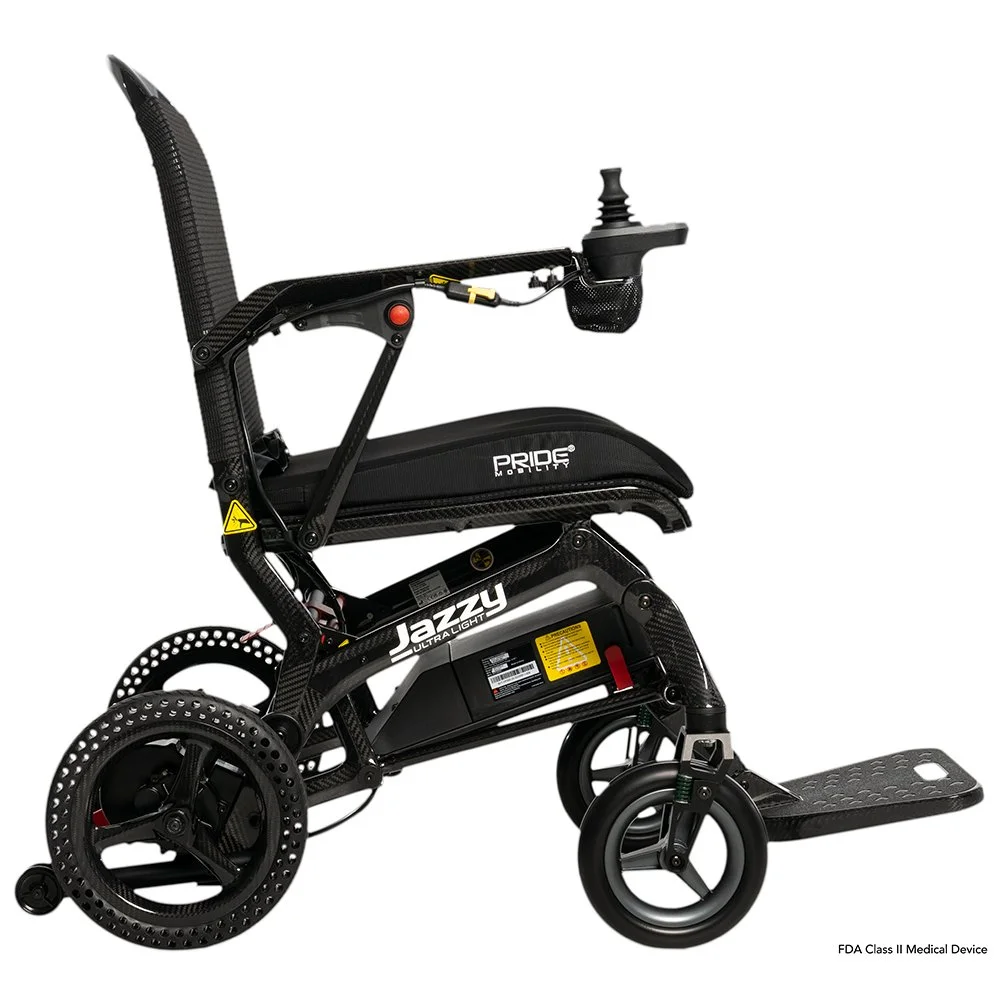 An electric wheelchair with a black frame, featuring small rear wheels, a footrest, and a seat with the brand "Pride Mobility."