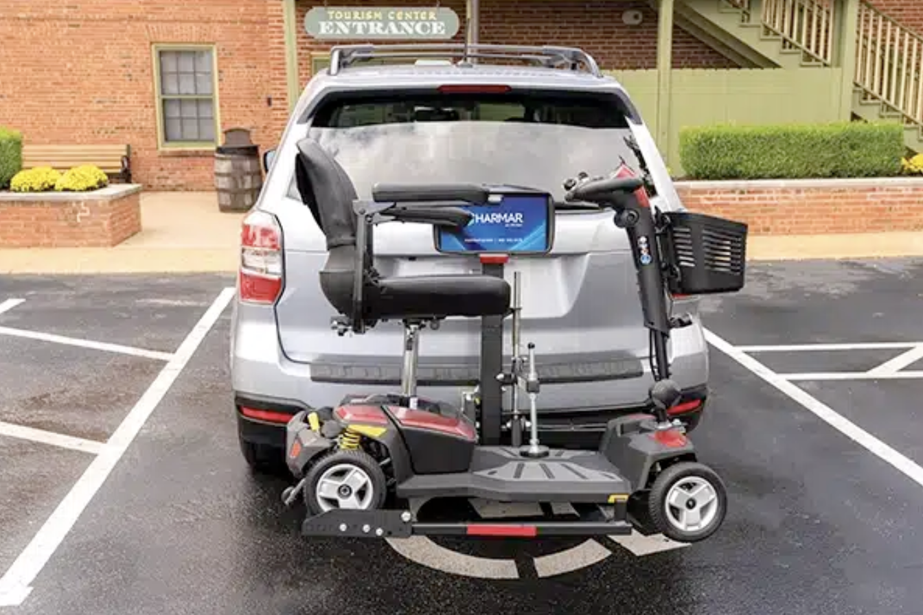 A silver SUV parked in a parking lot with a mobility scooter attached to the rear.