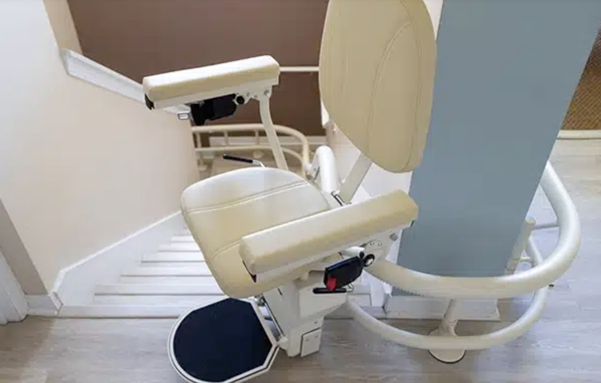 A beige medical recliner chair with armrests, a footrest, and safety belts, positioned next to a light blue wall in a medical facility.
