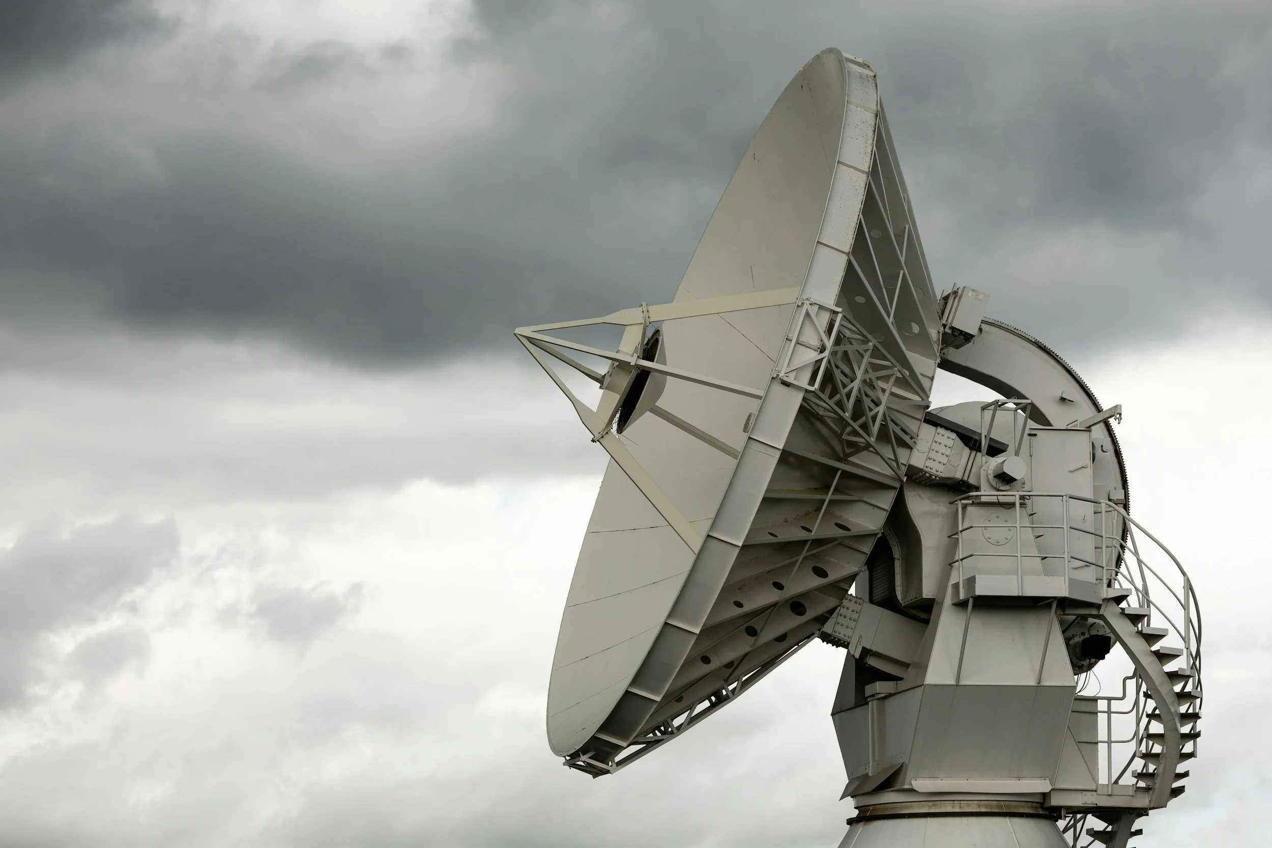 A large white satellite dish antenna pointing towards a cloudy sky.