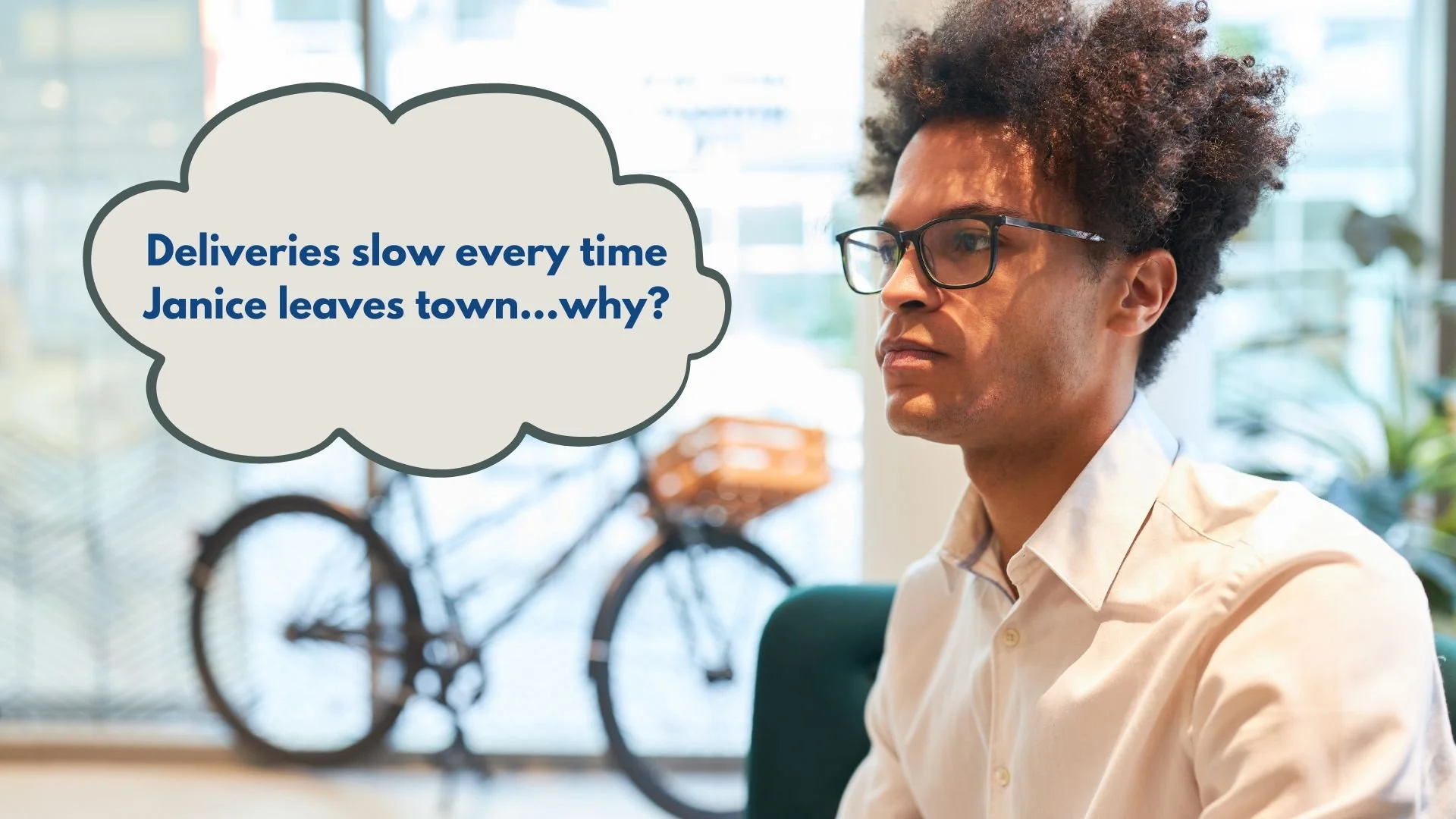 A man with curly hair, glasses, and a white shirt sitting indoors, with a bicycle visible in the background through a window. A speech bubble contains the text: "Deliveries slow every time Janice leaves town...why?".