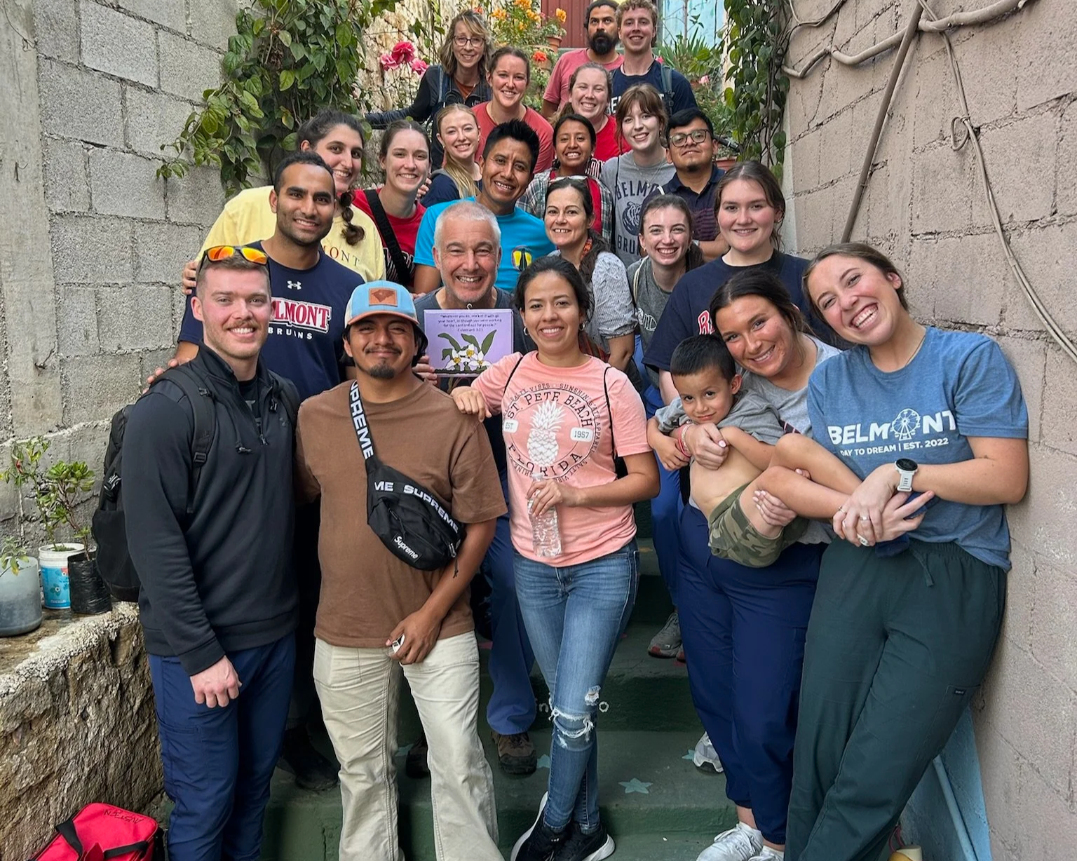 A large group of diverse smiling volunteers of various ages gathered on outdoor stairs at Centro Somos Futuros in San Andrez Itzapa.