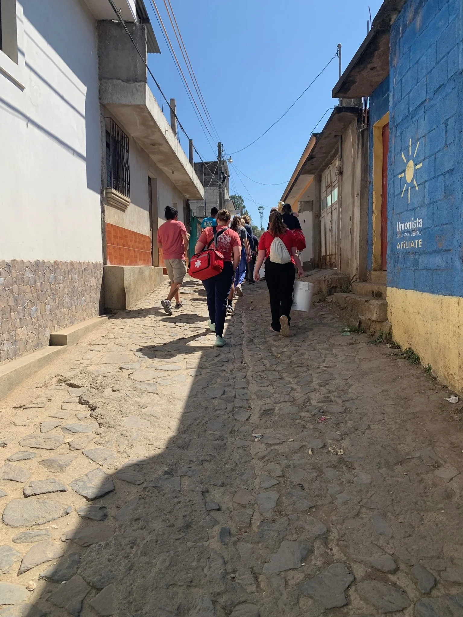 A group of volunteers walking up a narrow, cobblestone street in a small town in Guatemala to deliver bags of food to families.