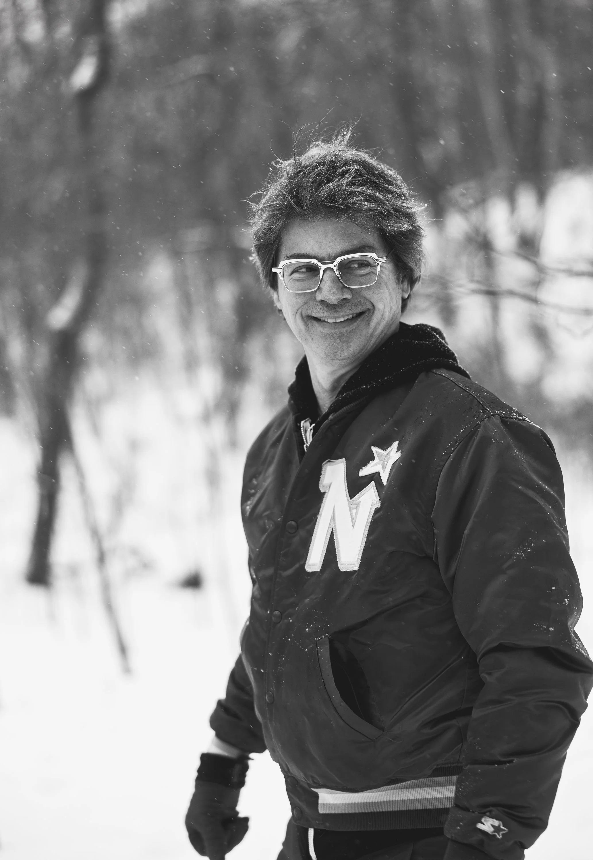 A man smiling outdoors in winter snow, wearing glasses and a jacket with a large letter 'Northstars' and star patch.