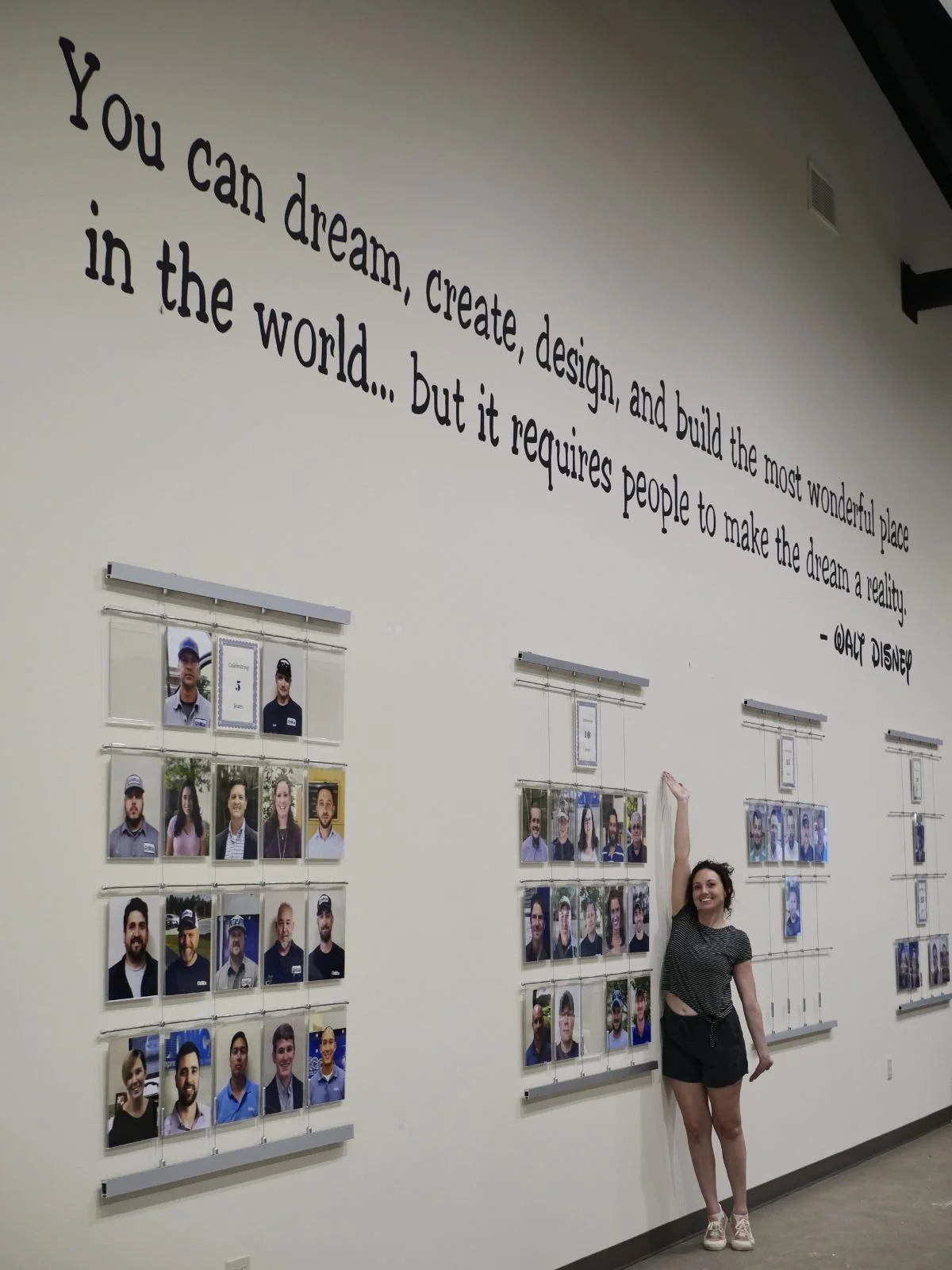 A woman standing in front of a wall with a quote and photos of people. The quote says, "You can dream, create, design, and build the most wonderful place in the world... but it requires people to make the dream a reality. - Walt Disney." The photos a