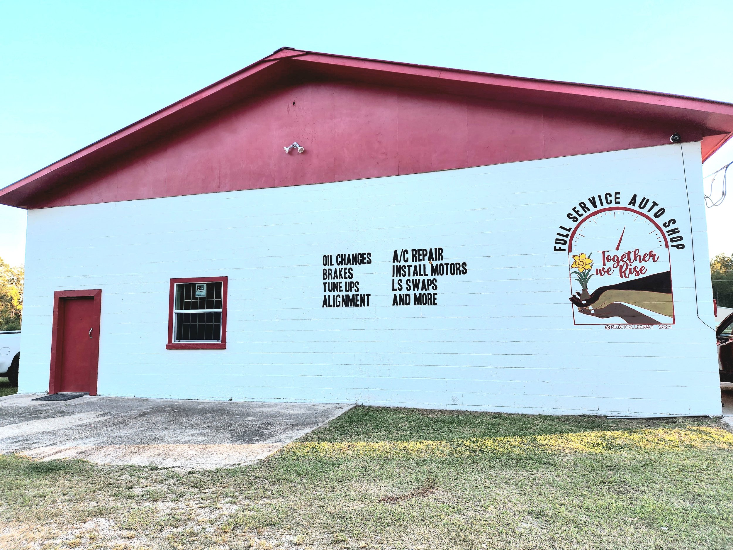 White building with red roof and door, black-outlined window, and a large sign advertising an auto repair shop with services like oil changes, brakes, tune-ups, A/C repair, and more. A circular logo reads 'Full Service Auto Shop' with a graphic of a 
