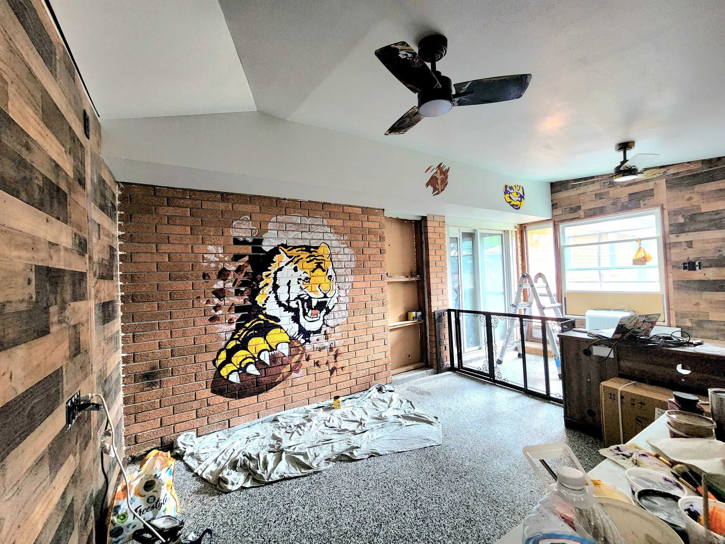 Interior room under renovation with painted tiger mural on brick wall, ladder, work materials, and windows.