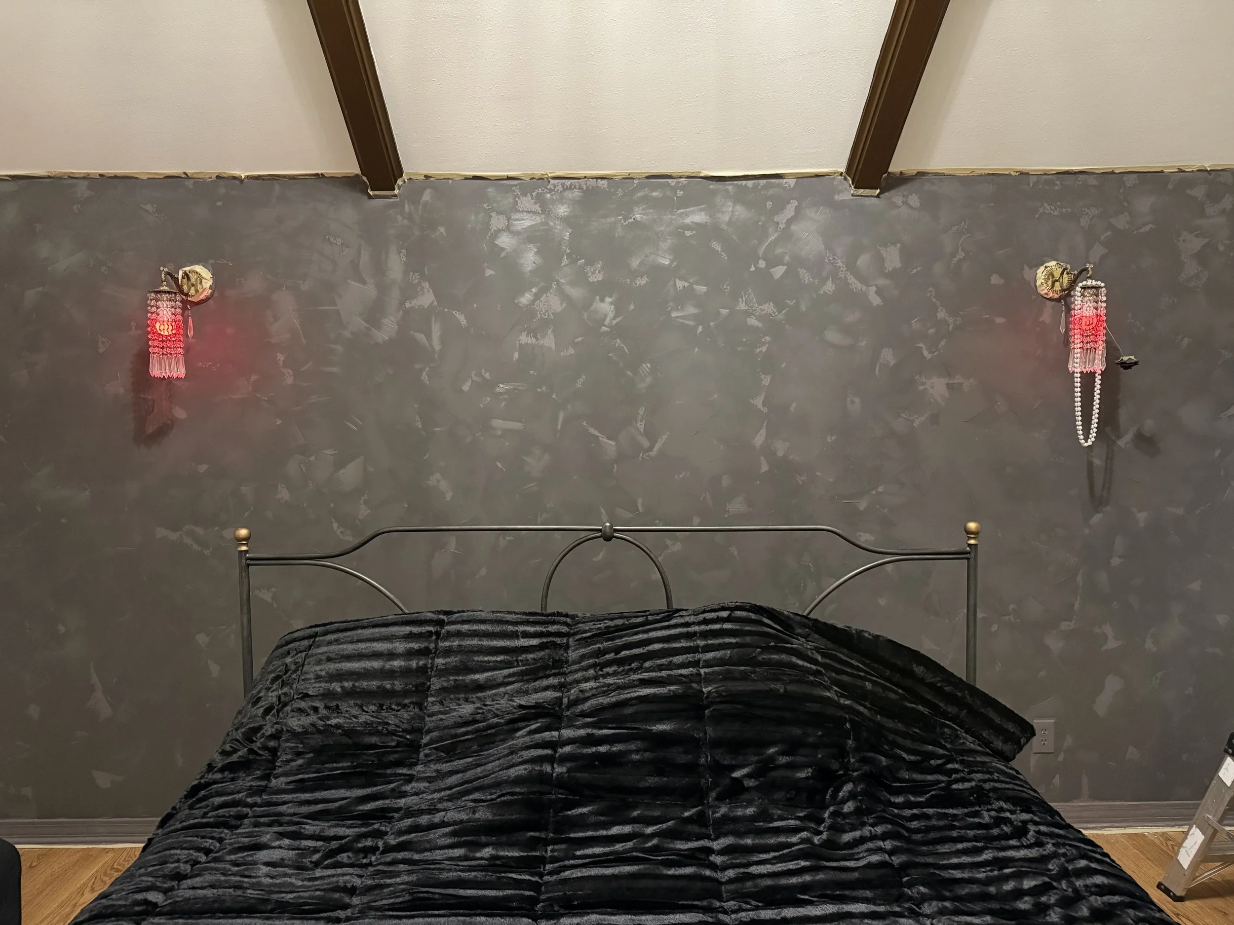 A bedroom with a black bedspread and two wall-mounted lamps with pink chains and decorations, viewed from above.