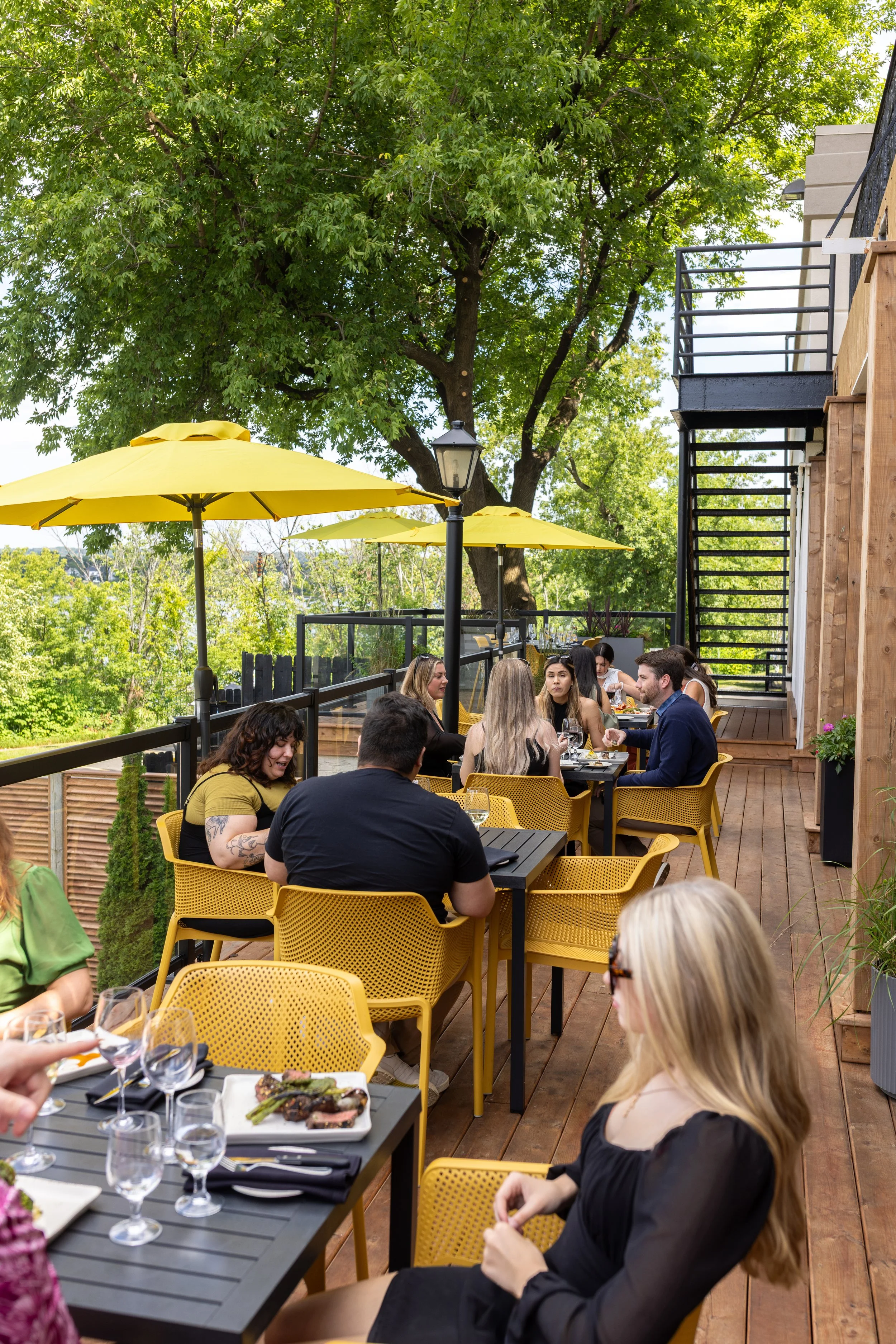 People dining at Maxwell's Steak & Seafood patio under yellow umbrellas with trees in the background.