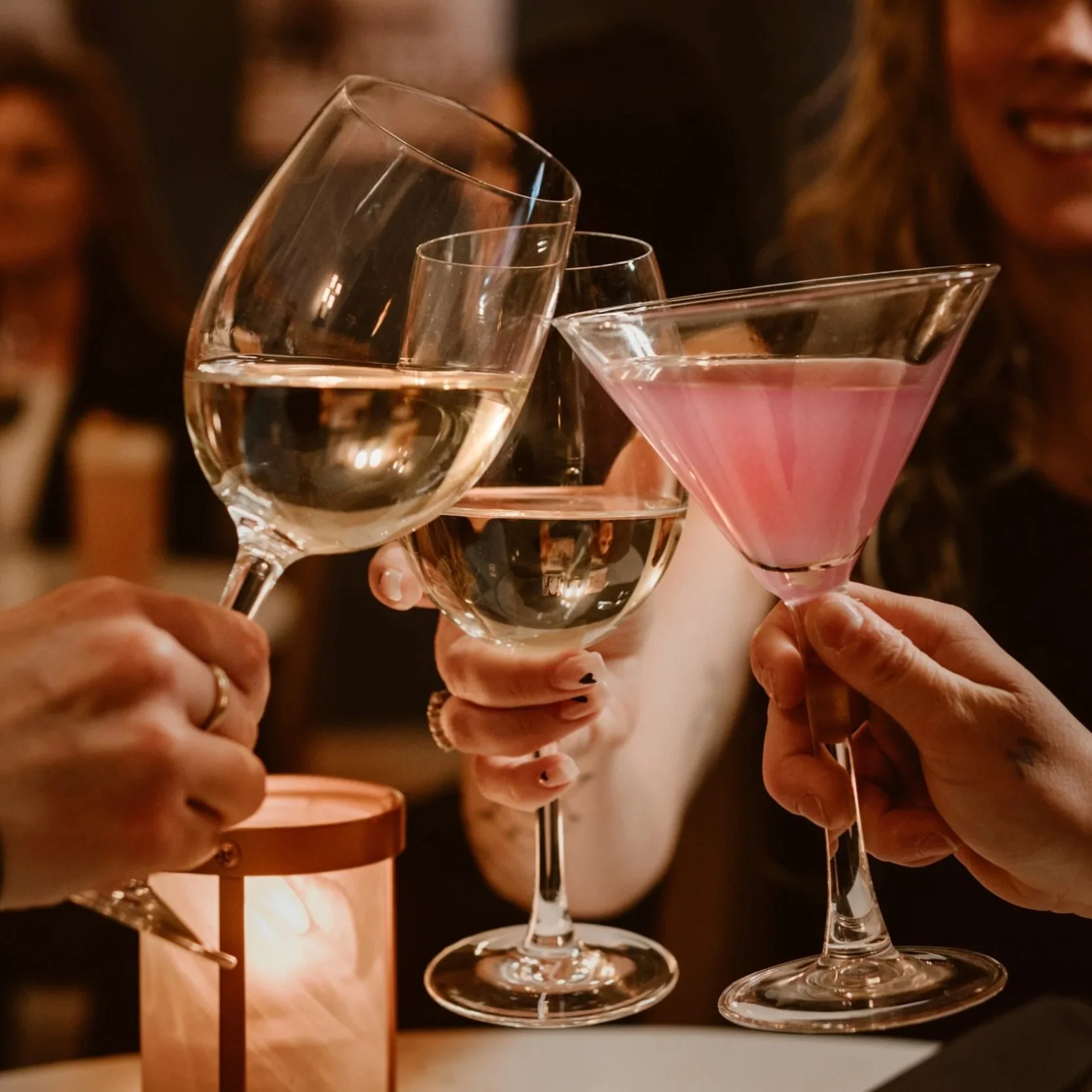 People clinking glasses with wine, champagne, and cocktail drinks in the cozy, warmly lit setting of Maxwell's Steak & Seafood.