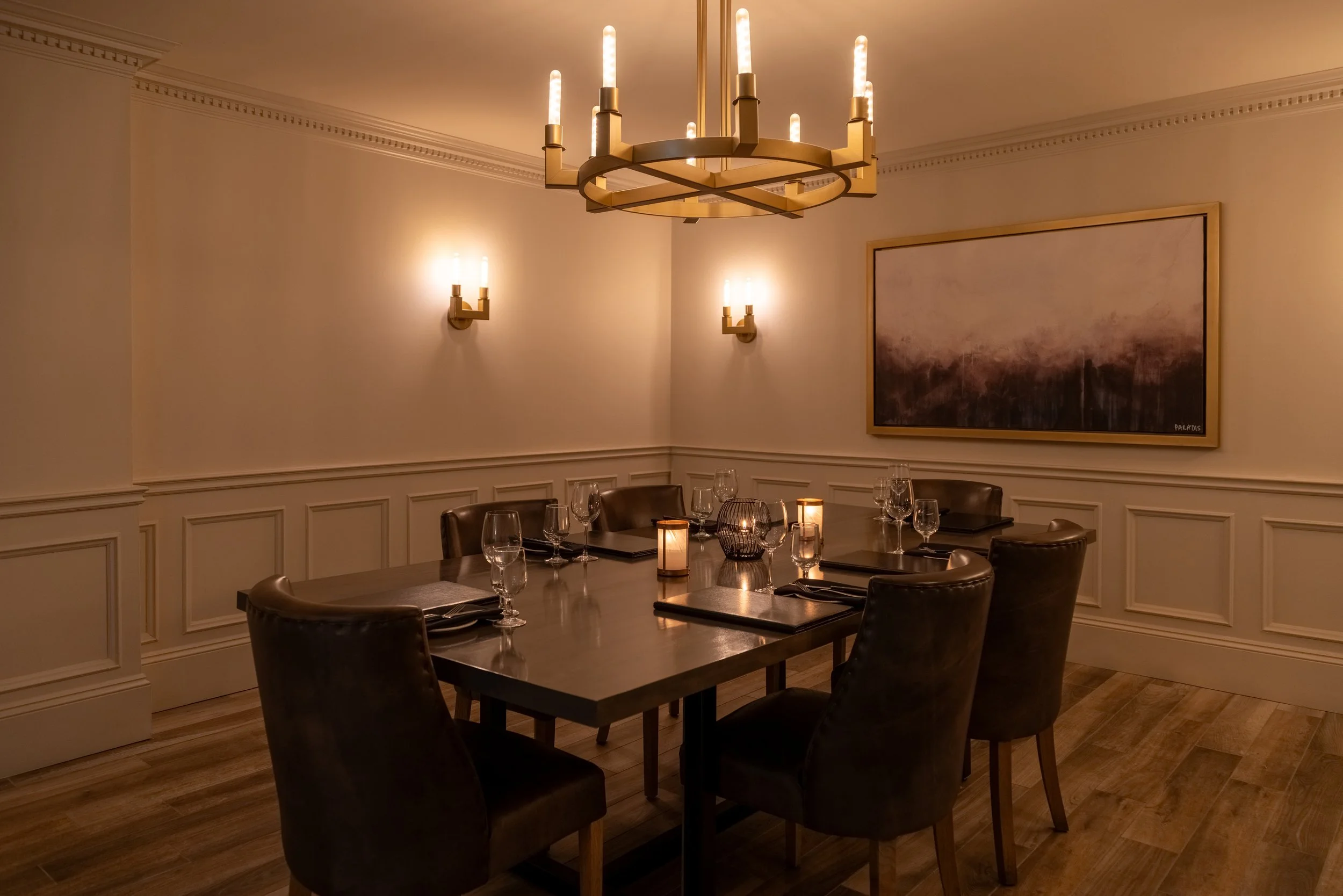 The dimly lit Websters room at Maxwell's Steak & Seafood with a rectangular wooden table, eight leather chairs, candles, wine glasses, and a large abstract painting on the wall.