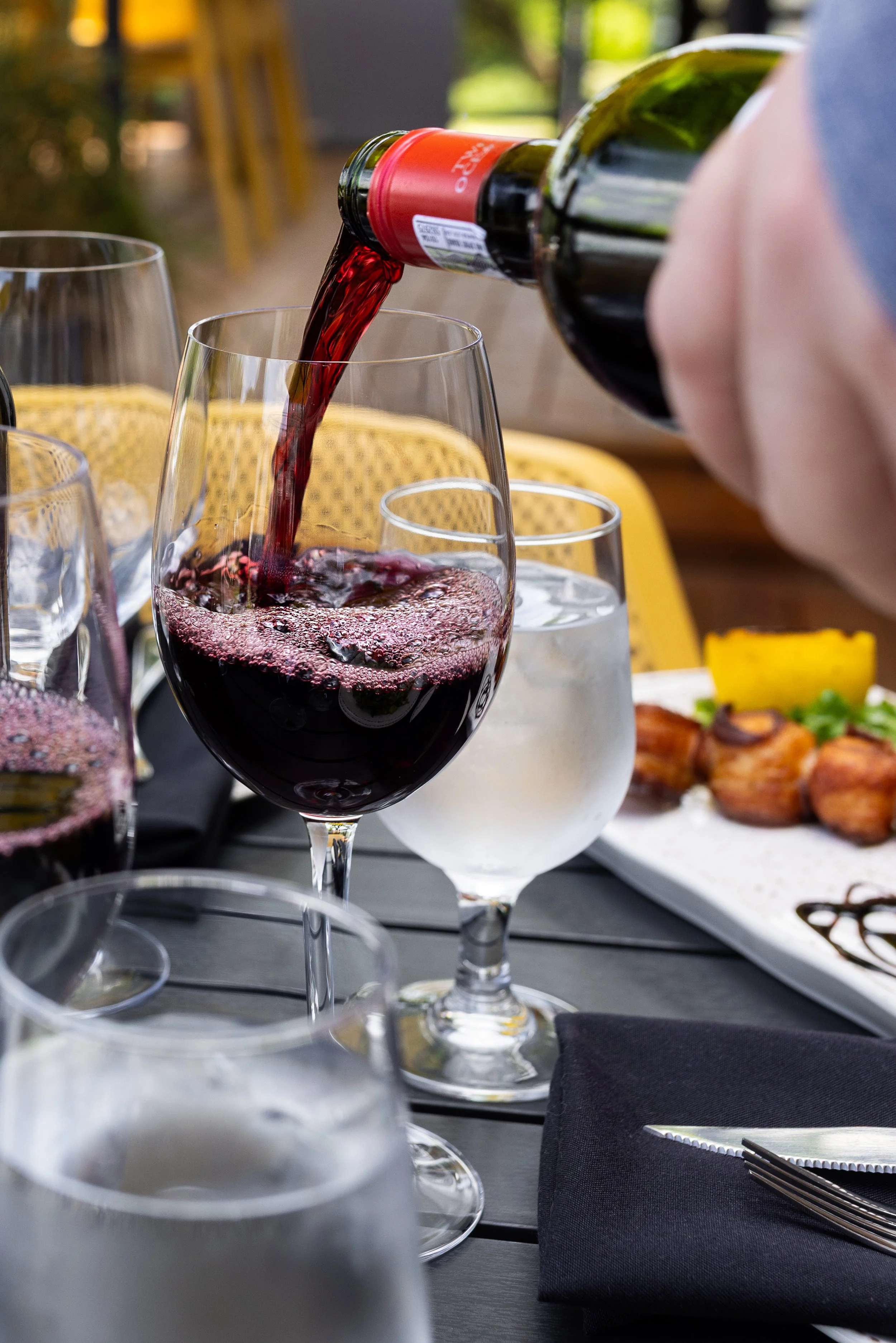 Red wine being poured into a glass at on a patio table at Maxwell's Steak & Seafood.