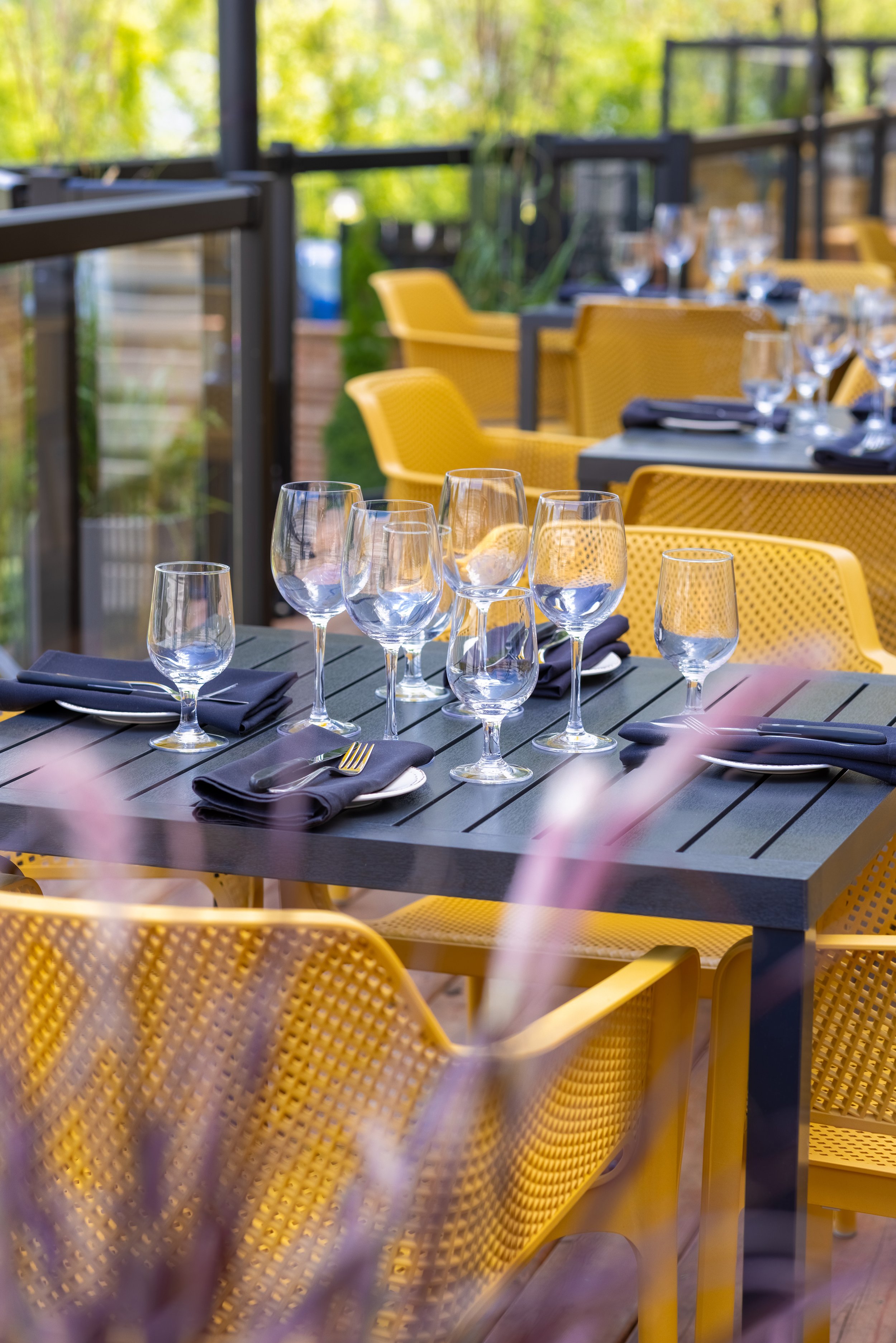 Maxwell's Steak & Seafood patio table set with wine glasses, plates, black napkins, and silver utensils, surrounded by yellow chairs.