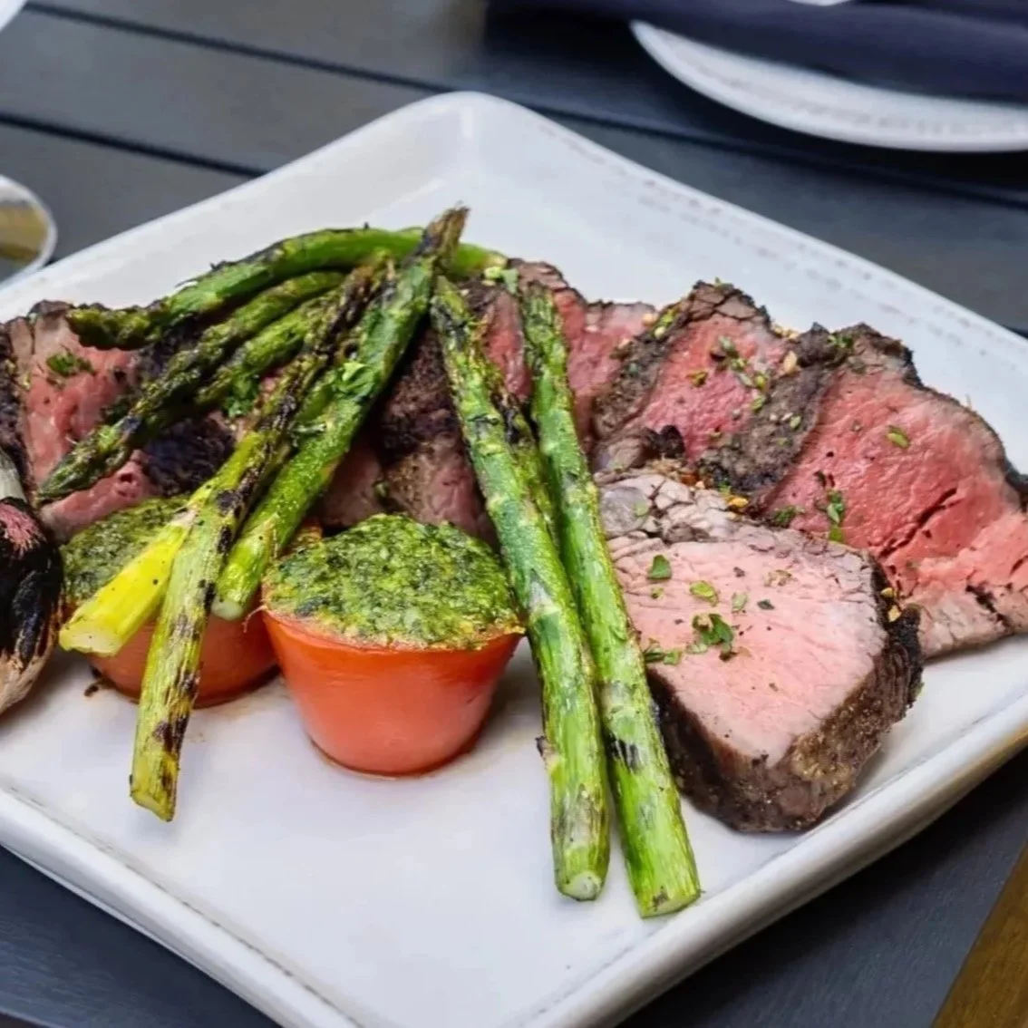 Maxwell's Steak & Seafood's steak with roasted asparagus and a baked tomato on a white plate.