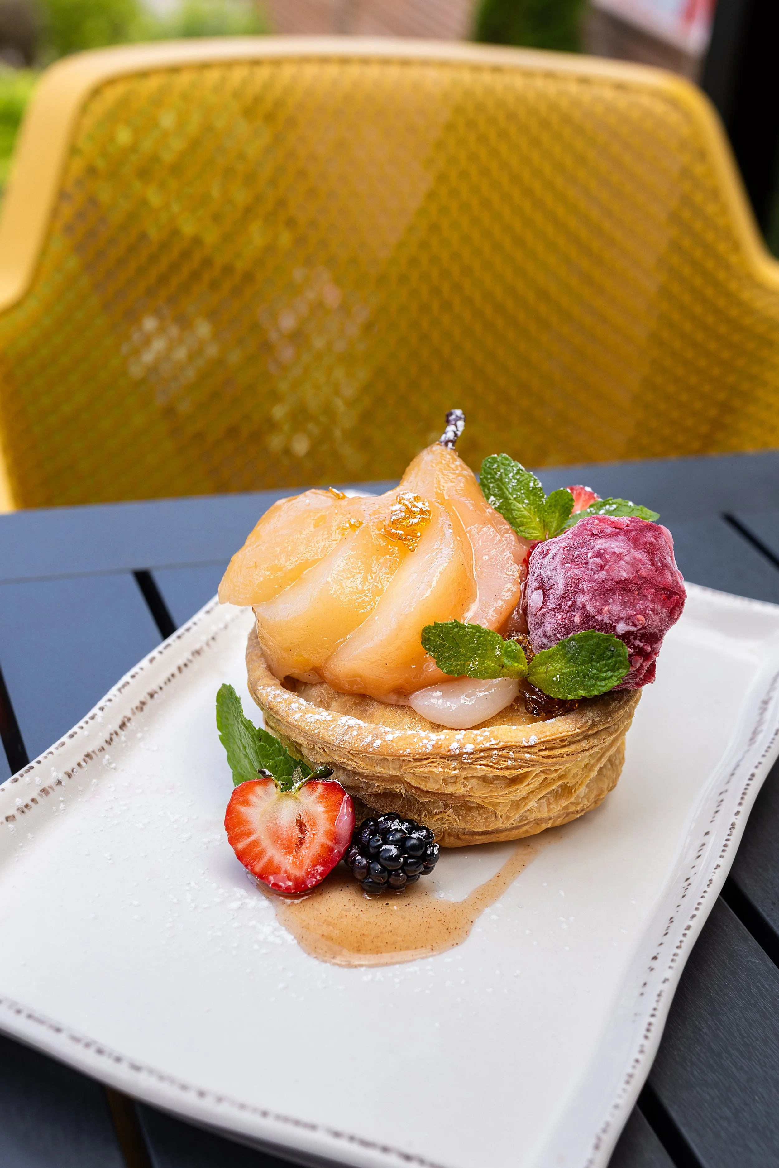 Fruit tart topped with pear, strawberry, blackberry, raspberry, mint leaves, dusted with powdered sugar, on a white plate served on the patio table of Maxwell's Steak & Seafood.